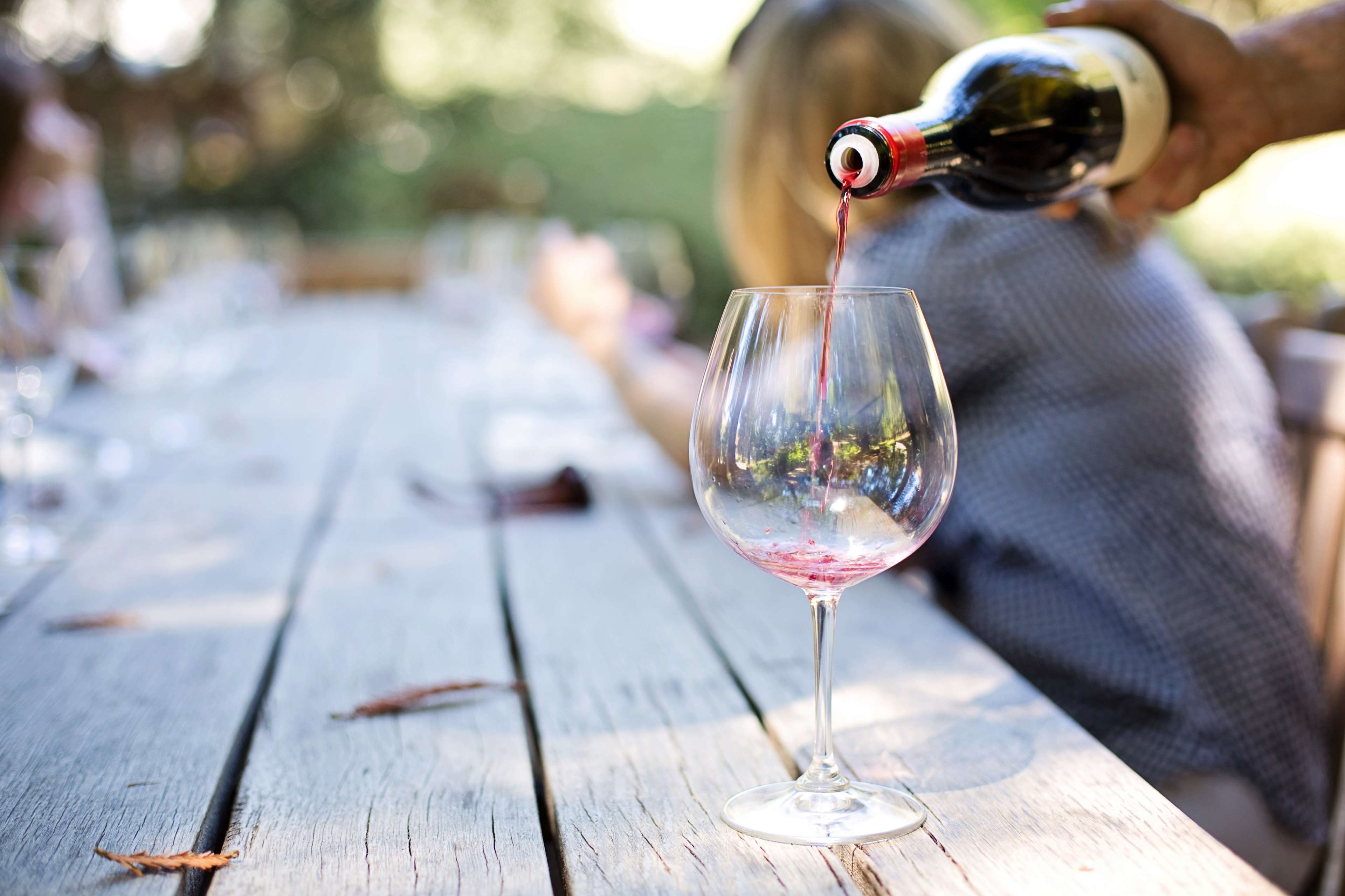 Wine being poured into a glass at an outdoor table HD Wallpaper