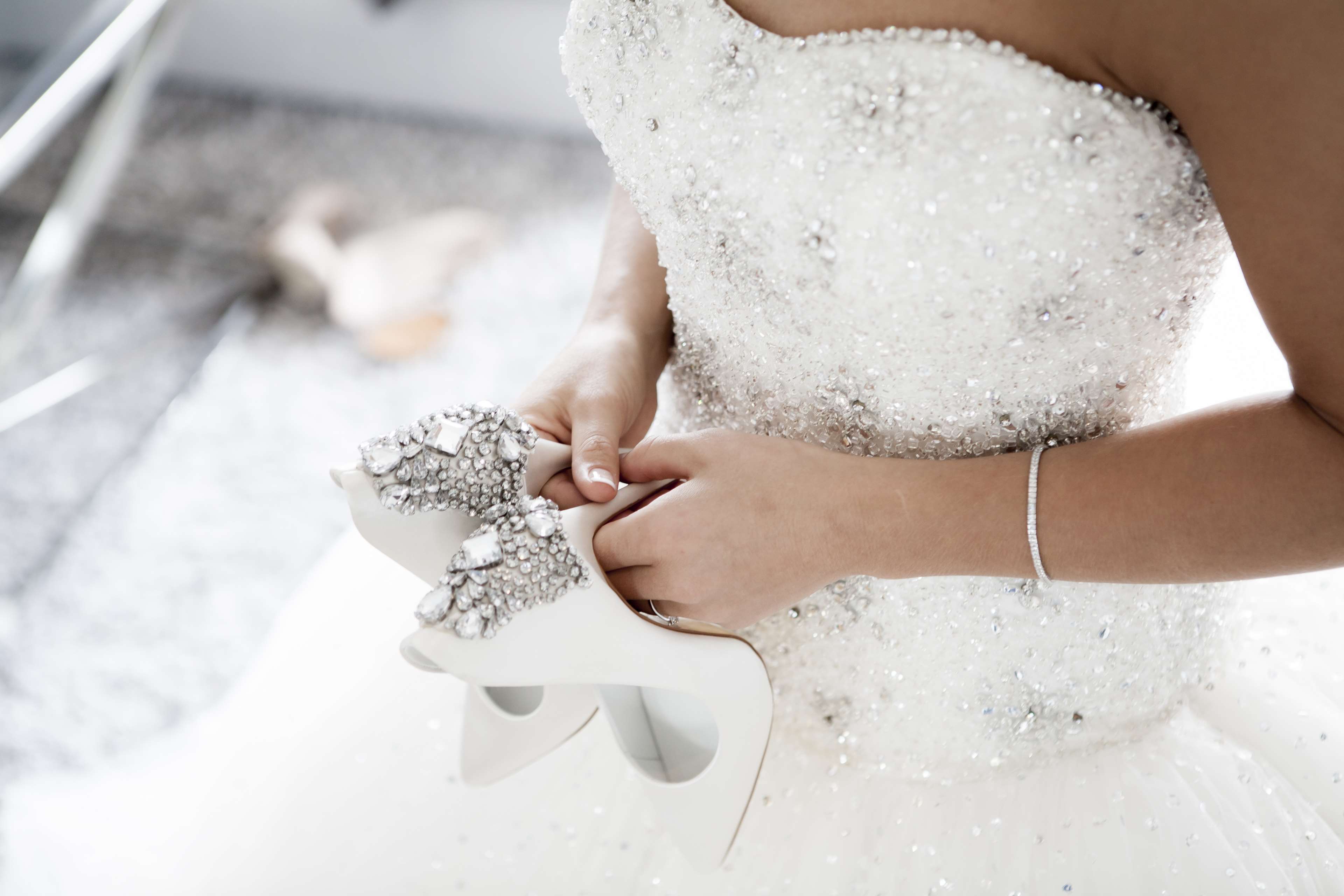 Bride holding embellished high heels, wearing a sparkling wedding dress HD Wallpaper