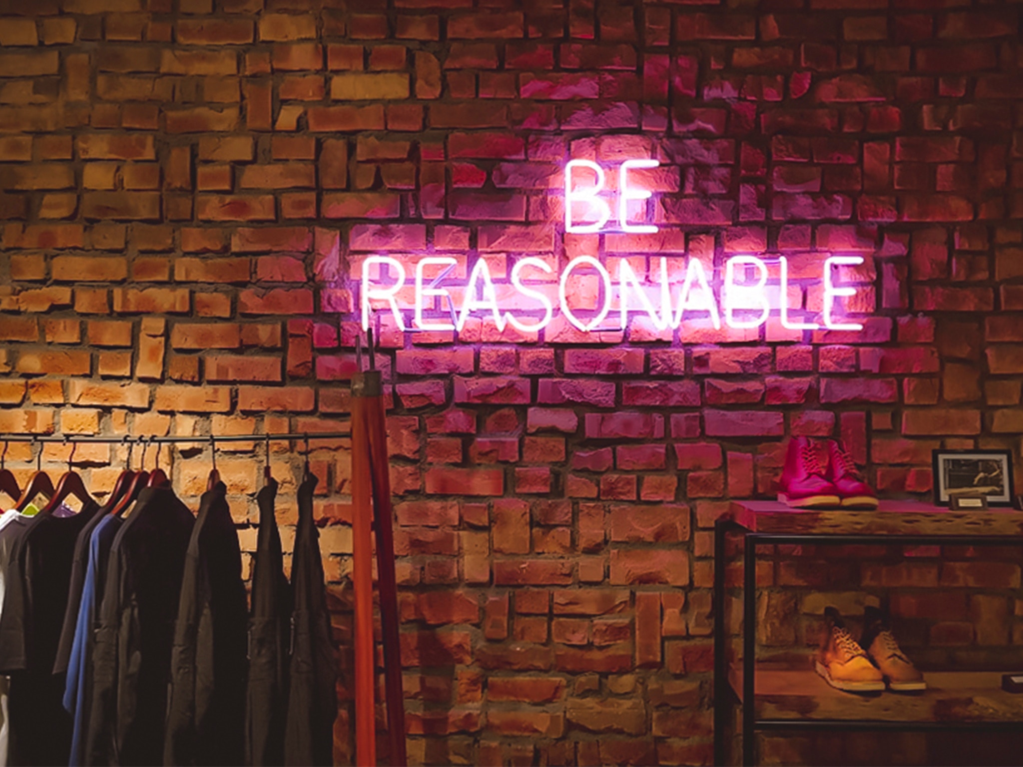 Neon sign "BE REASONABLE" on a brick wall HD Wallpaper