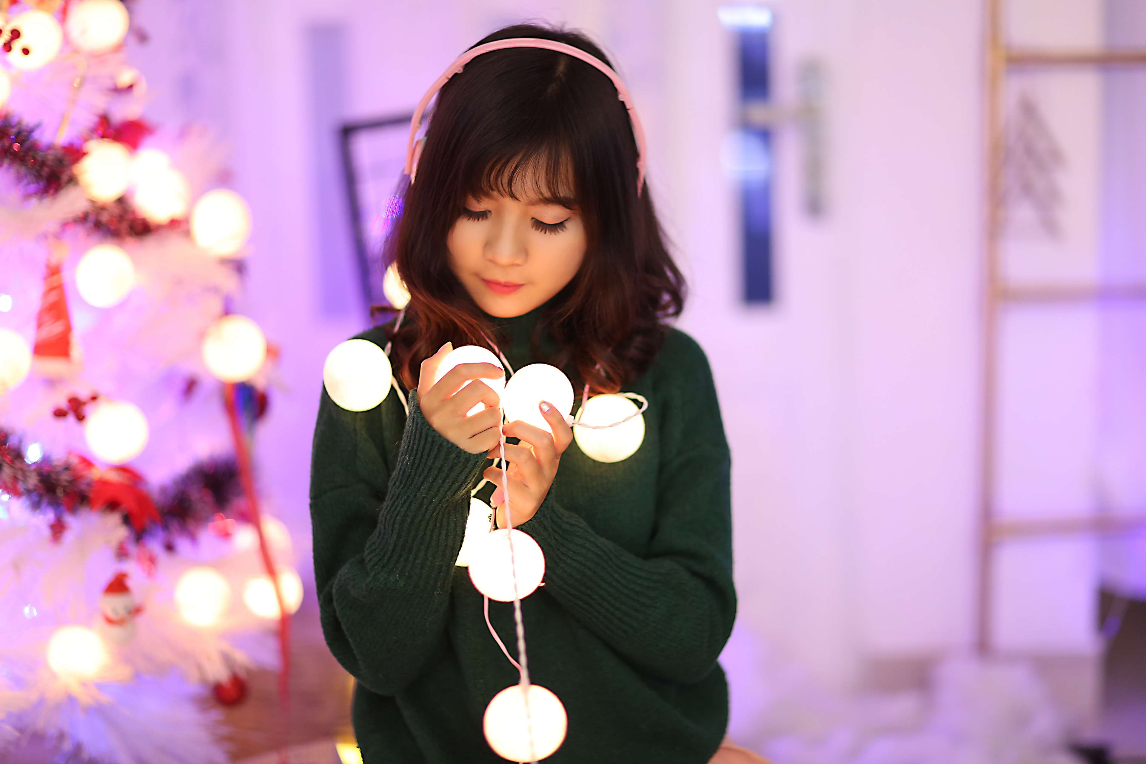 Young woman with headphones holding Christmas lights HD Wallpaper