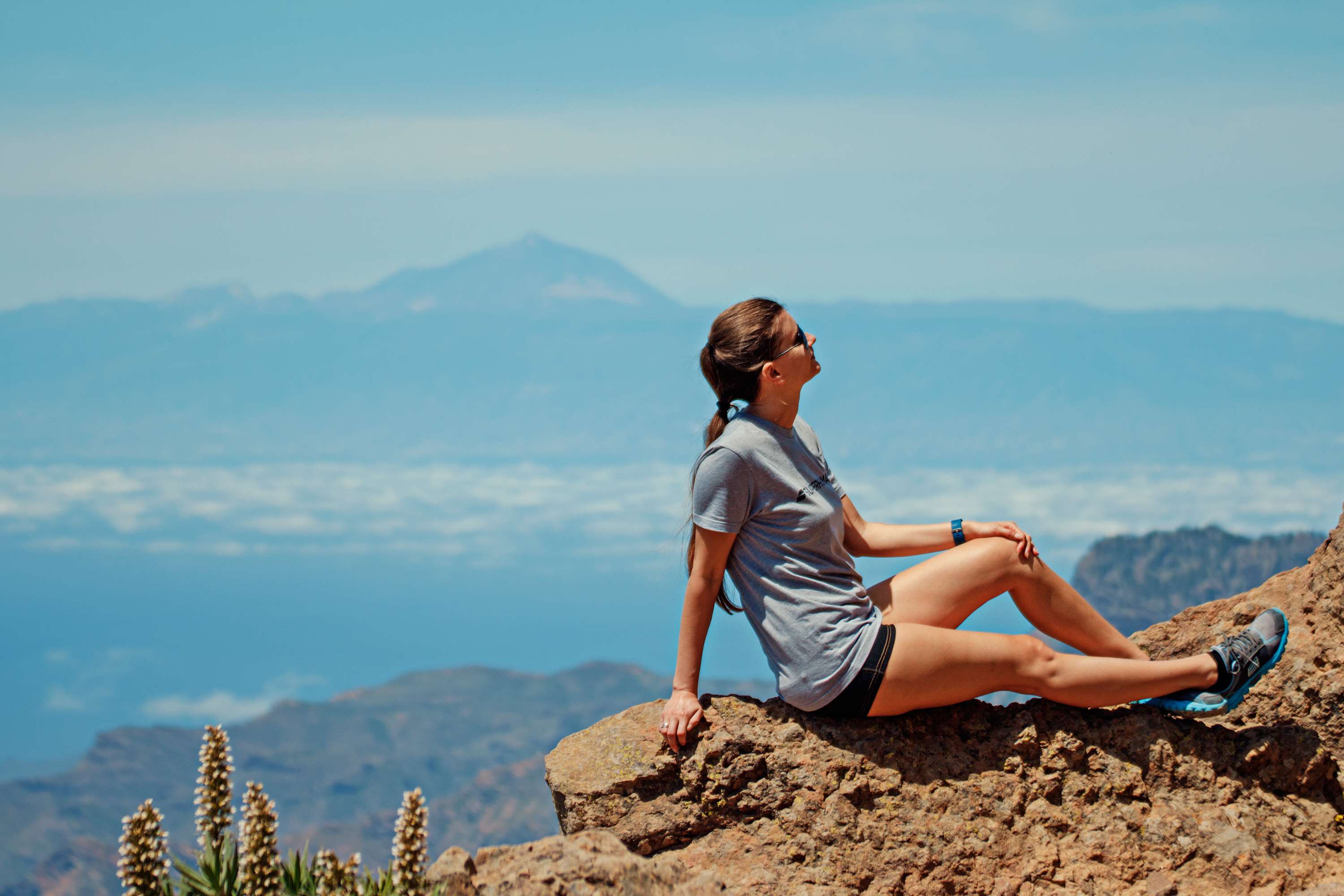 Woman sitting on rocks overlooking mountains and clouds HD Wallpaper
