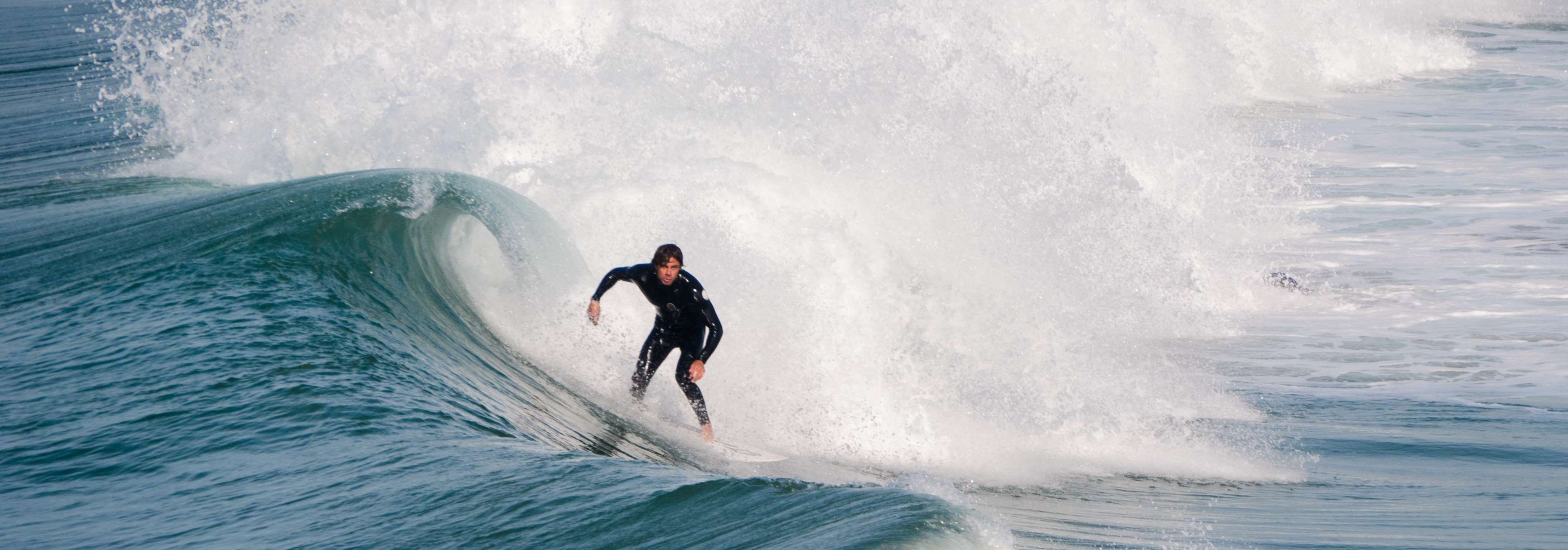 Surfer riding a wave in a wetsuit HD Wallpaper