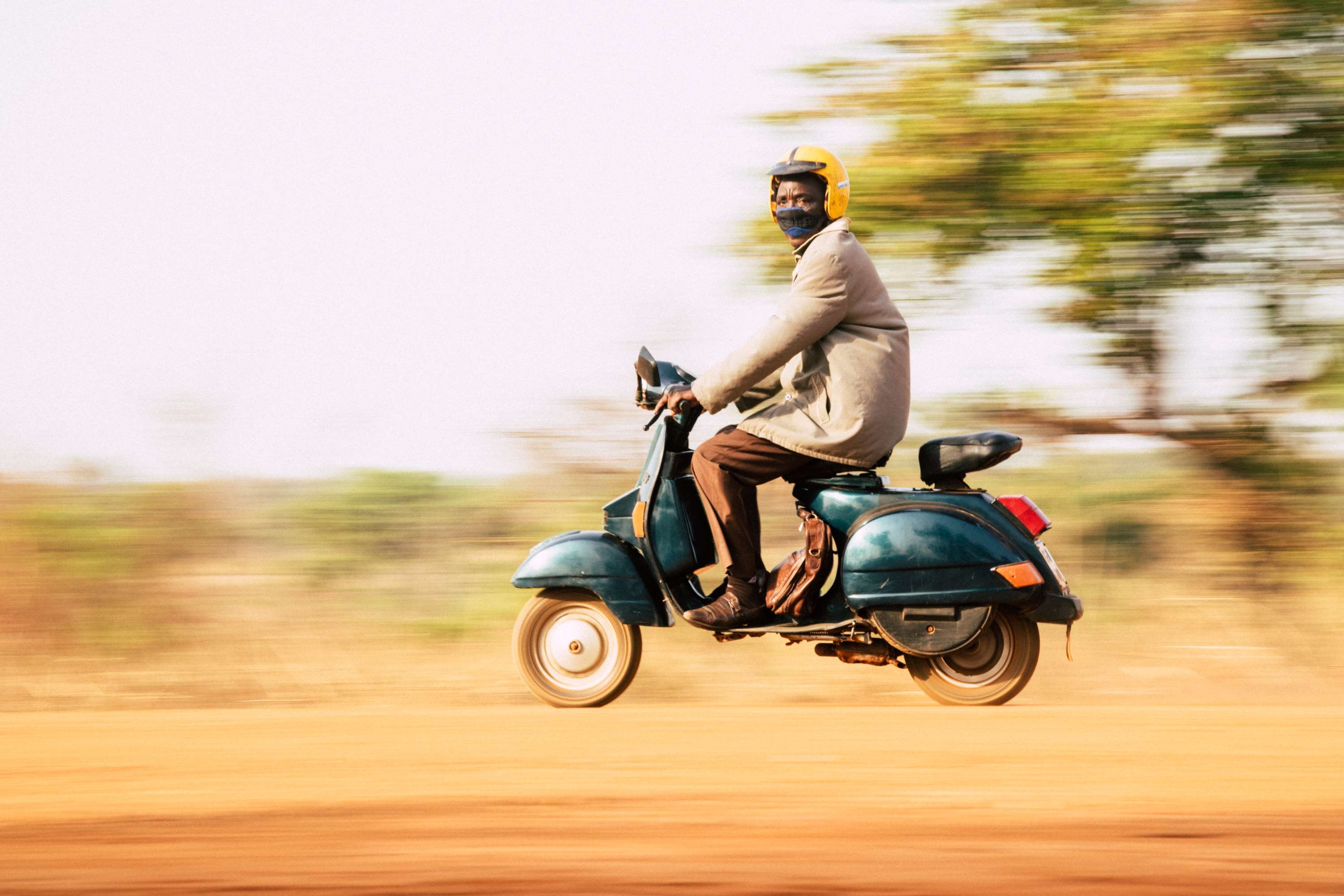 Man in yellow helmet riding a scooter in Africa HD Wallpaper