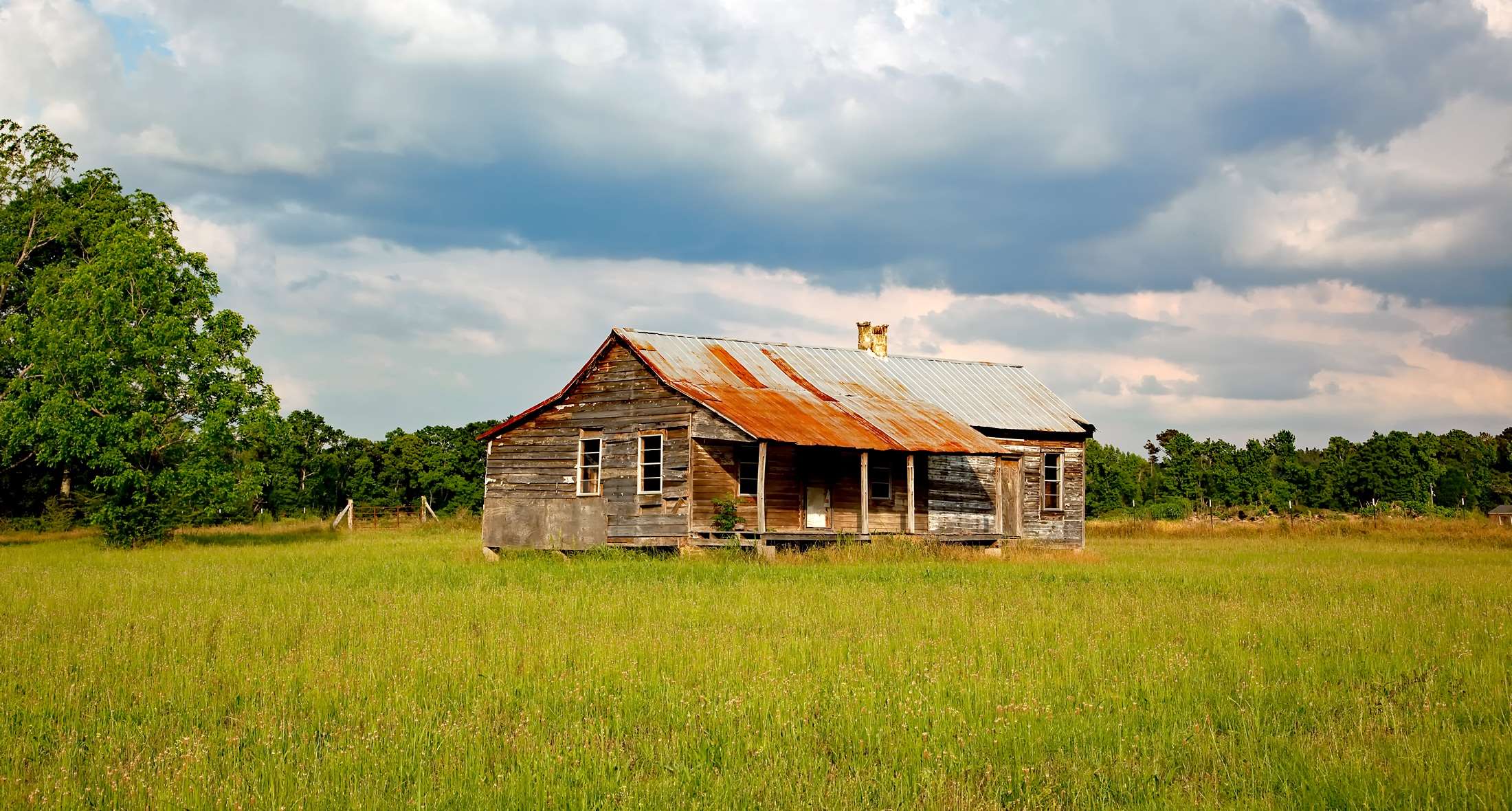Abandoned farmhouse in a grassy field under cloudy sky HD Wallpaper