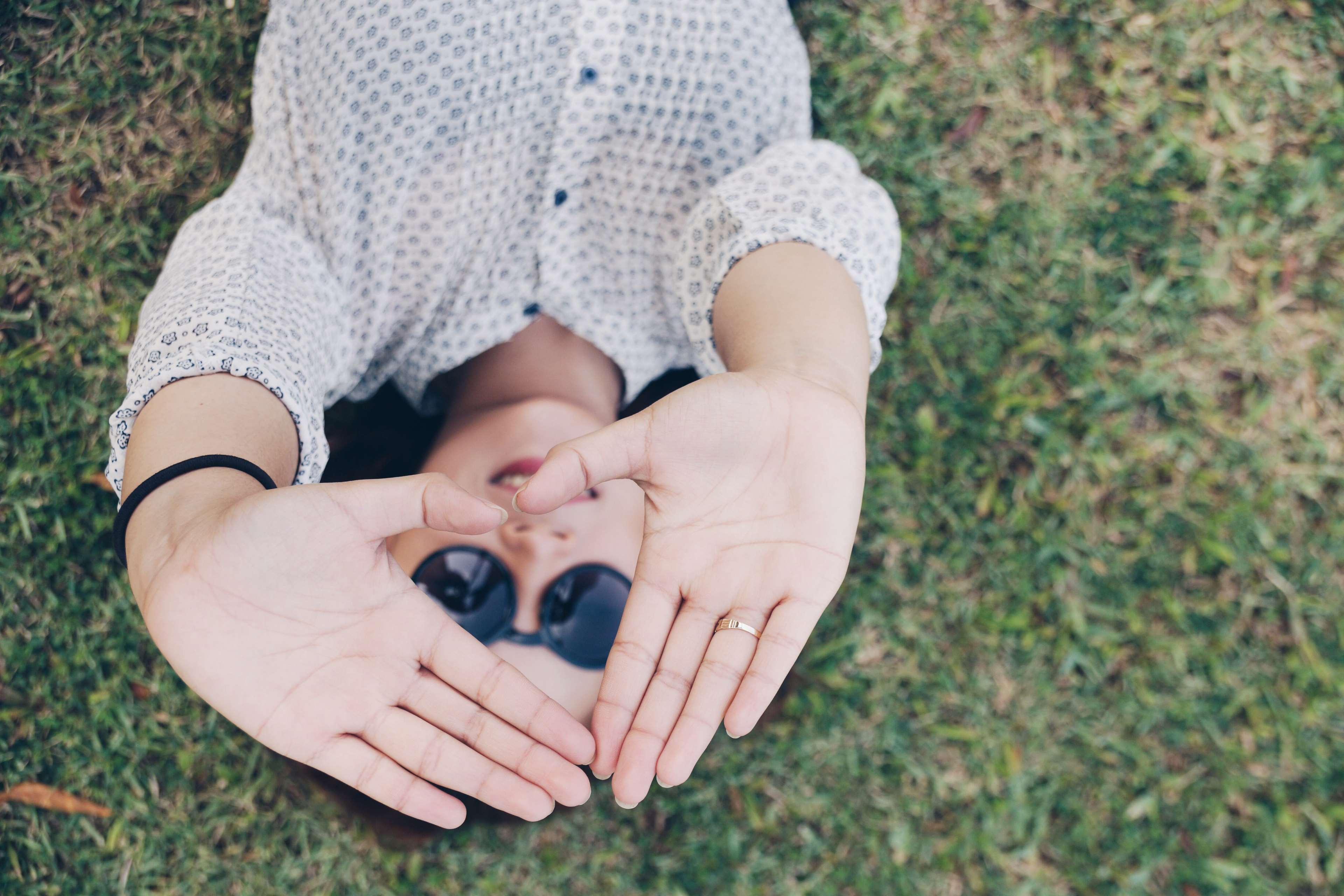 Woman lying on grass making heart shape with hands HD Wallpaper