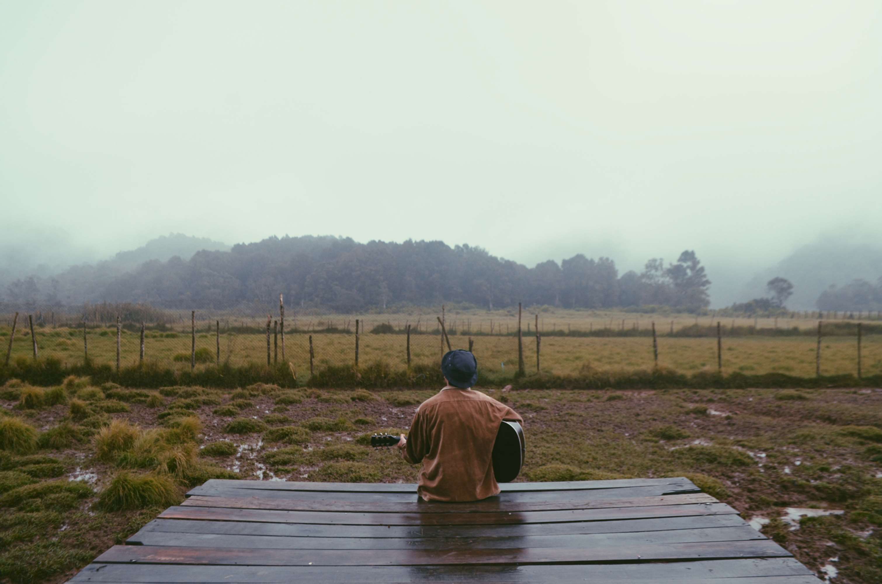 Man playing guitar on wooden platform in foggy landscape HD Wallpaper