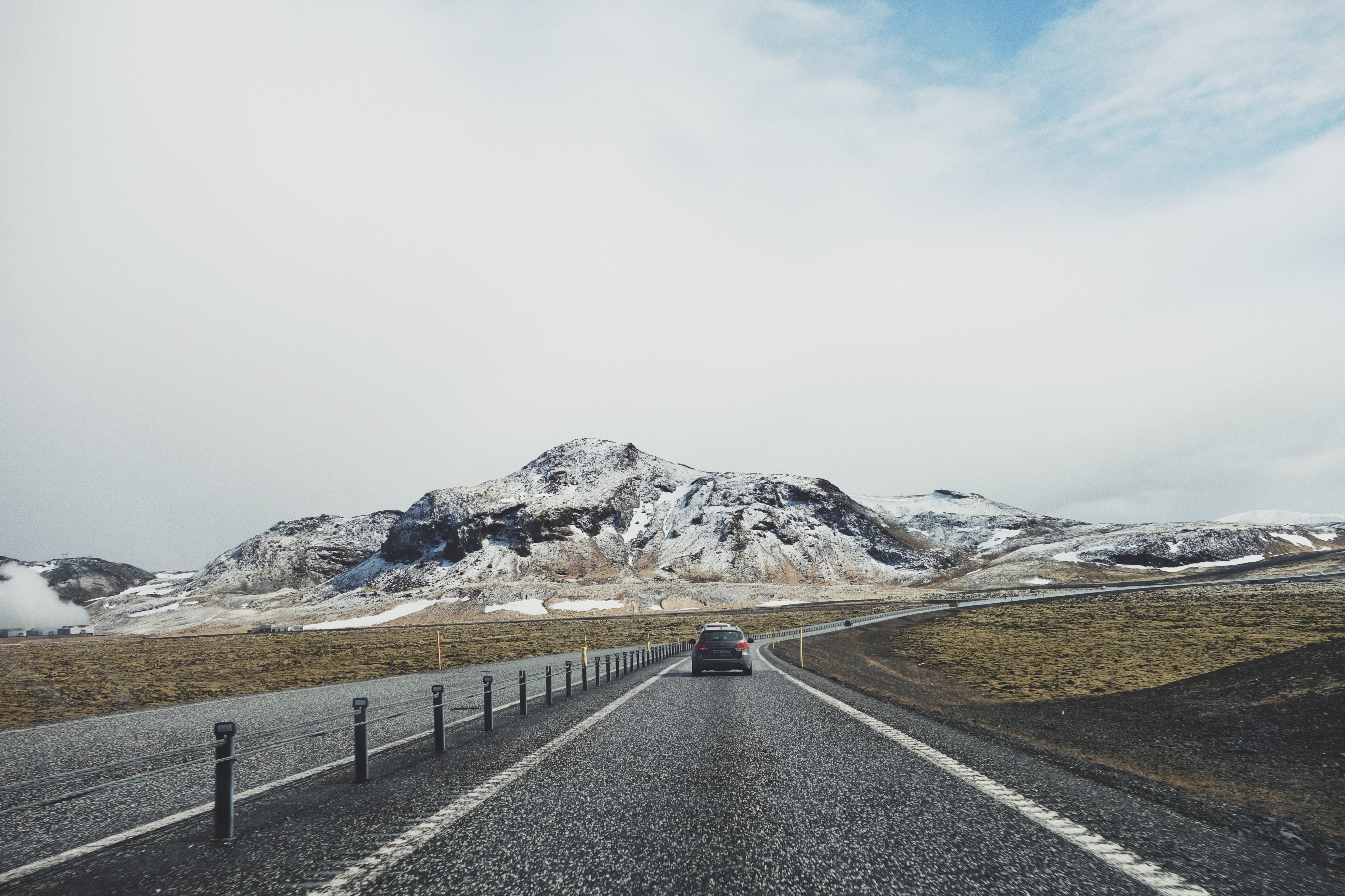 Car driving on a road towards a snow-covered mountain in Iceland HD Wallpaper