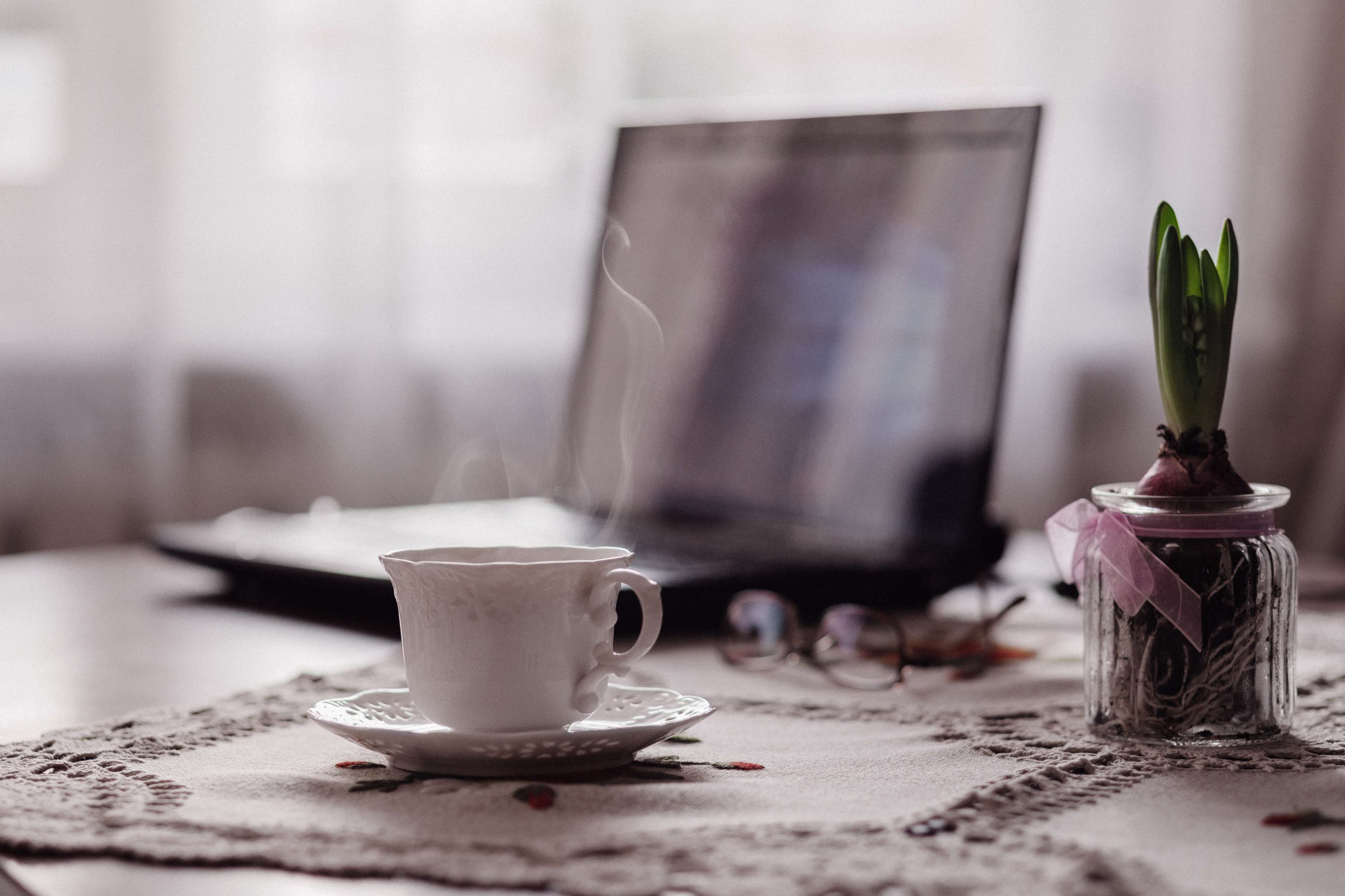 Steaming cup of coffee on a table with a laptop and plant HD Wallpaper