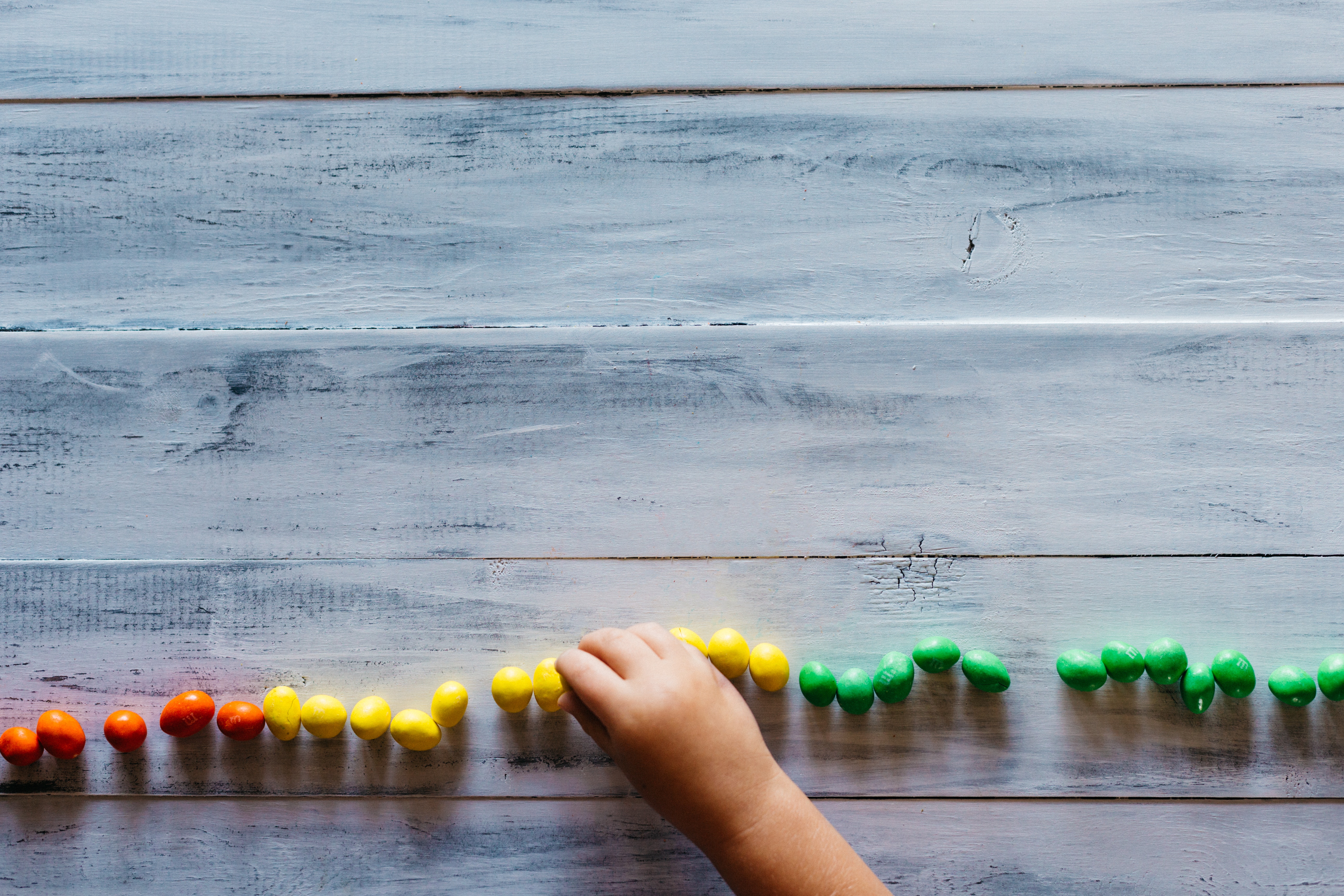 Child's hand arranging colorful candies on a wooden table HD Wallpaper