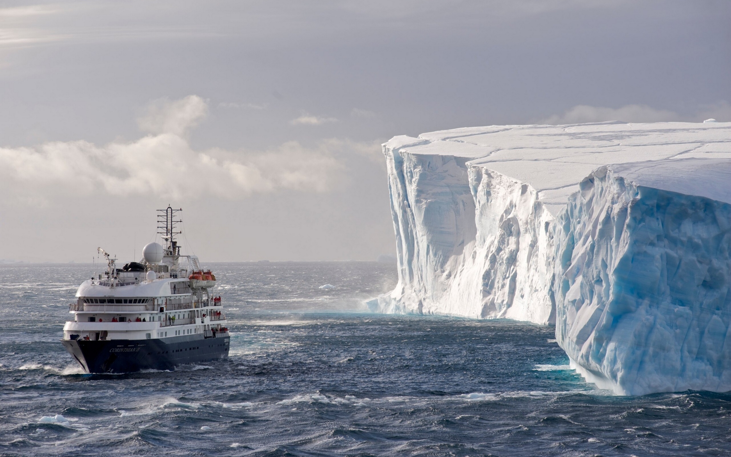 Cruise ship sailing near a large iceberg in Antarctica HD Wallpaper