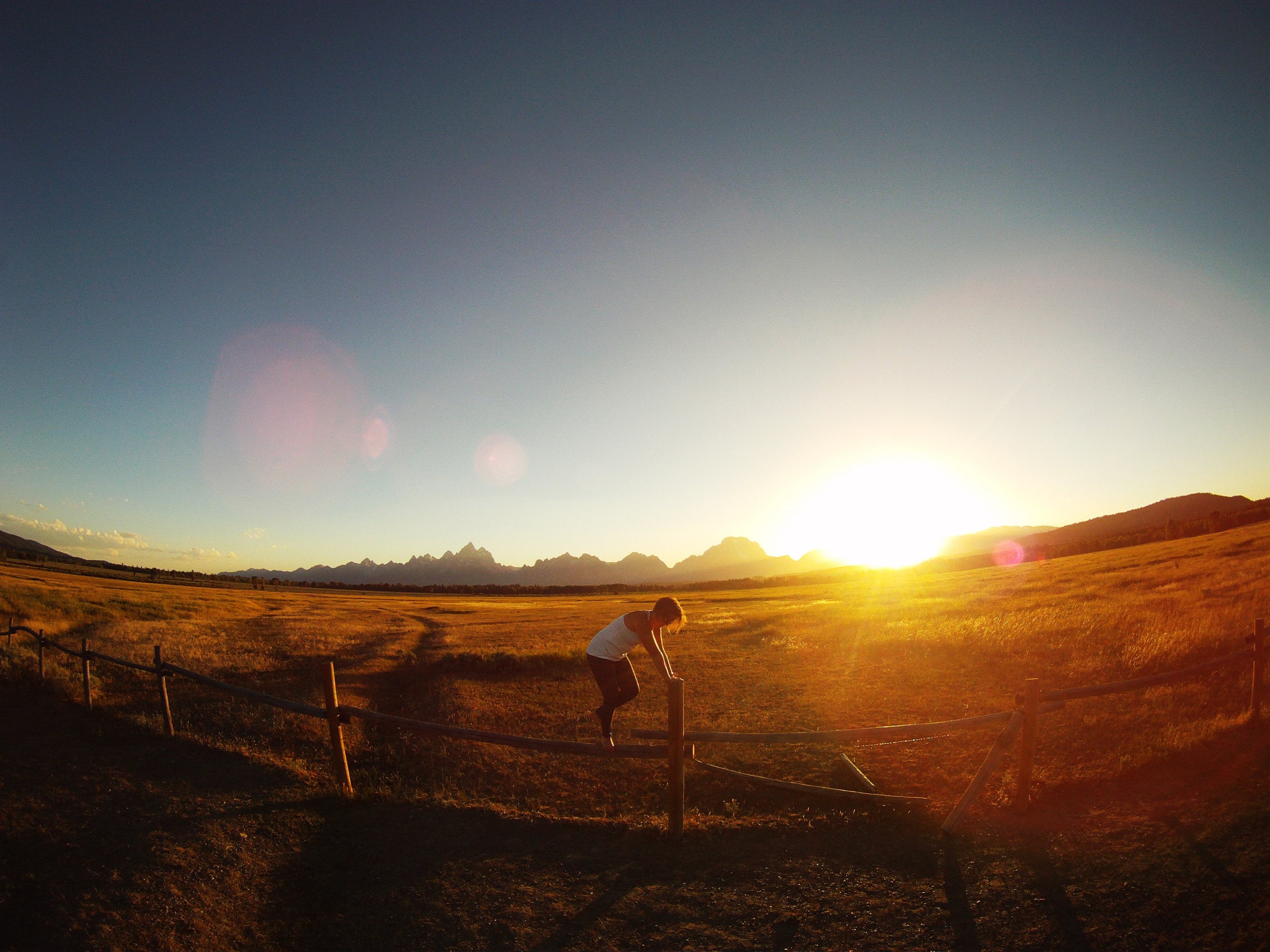 Person jumping over a fence at sunset with mountains HD Wallpaper