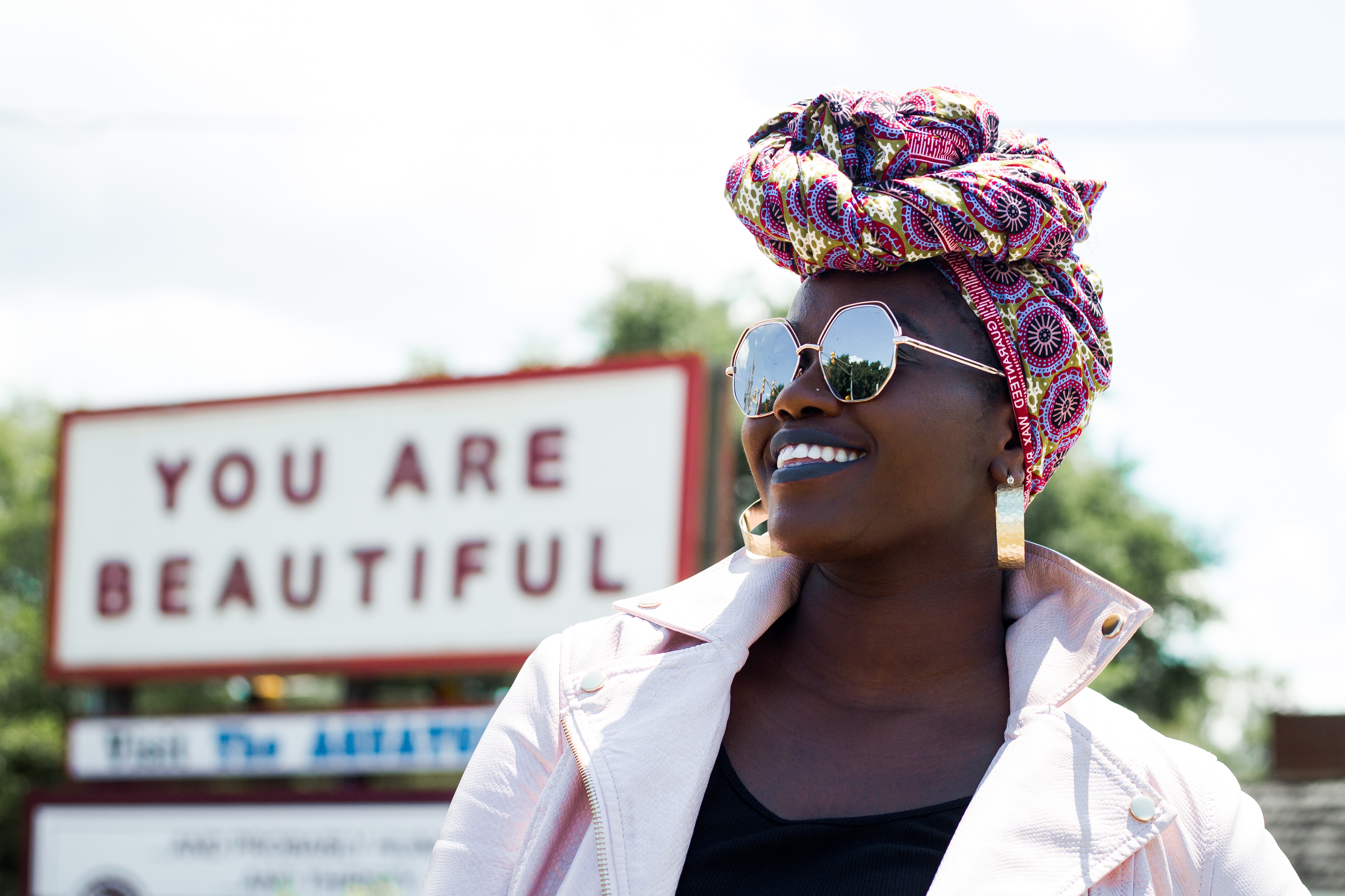 Woman wearing a turban and sunglasses in front of a sign HD Wallpaper