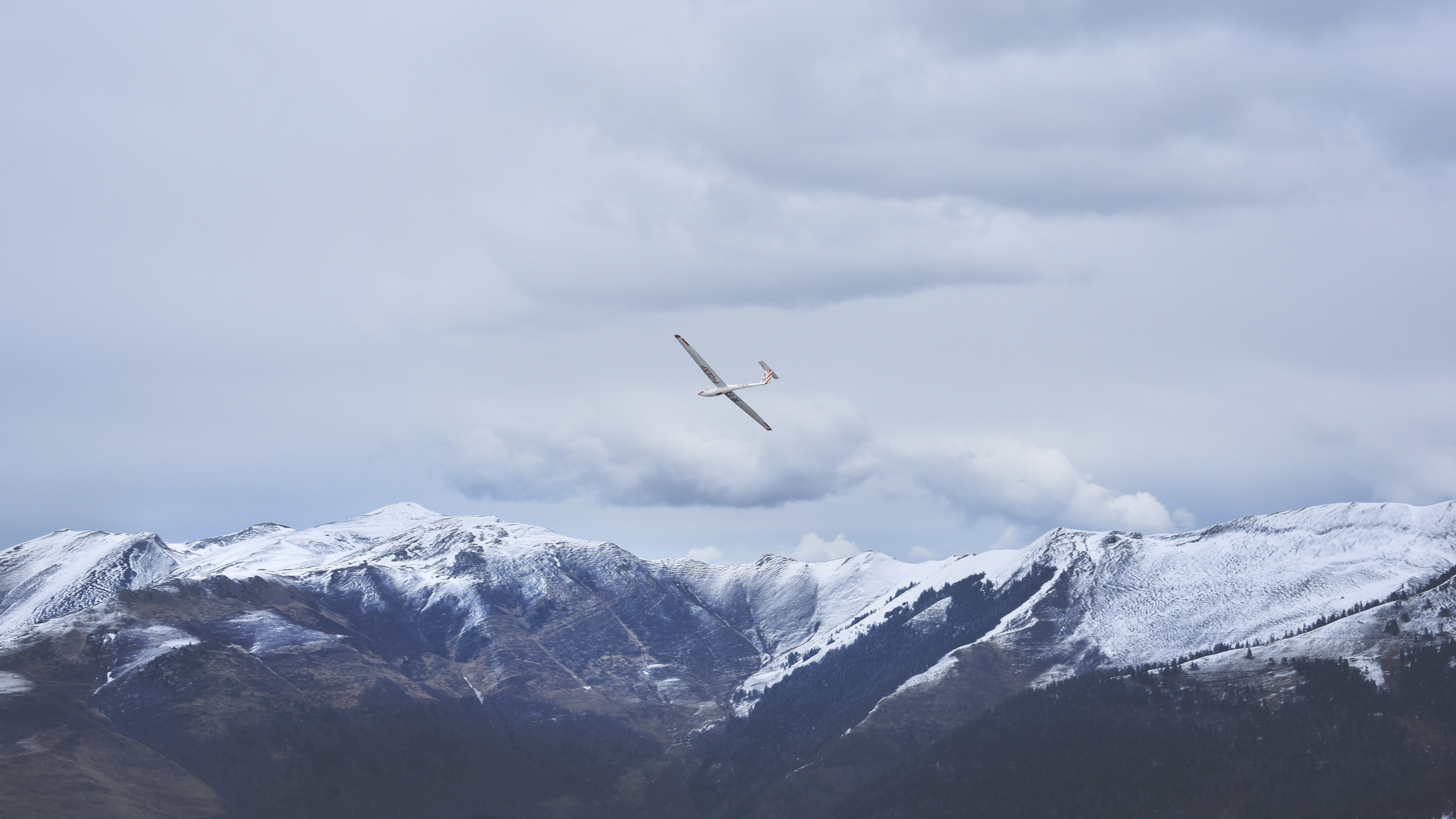 Glider plane flying over snow-capped mountains HD Wallpaper