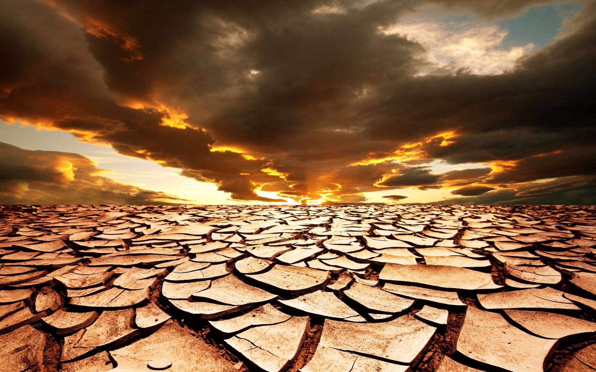 Cracked earth under a dramatic sunset sky HD Wallpaper