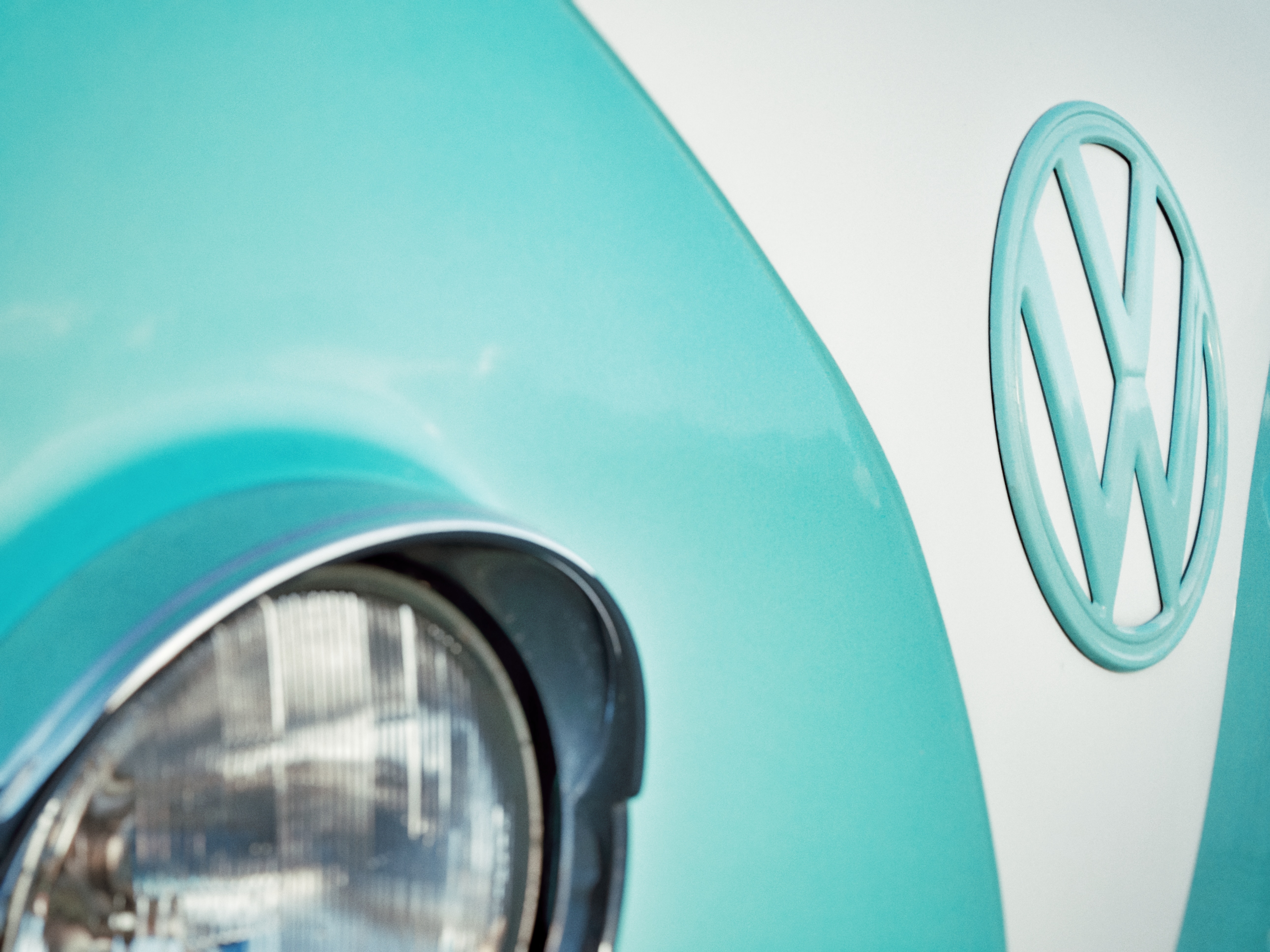 Close-up of a turquoise and white Volkswagen logo and headlight HD Wallpaper