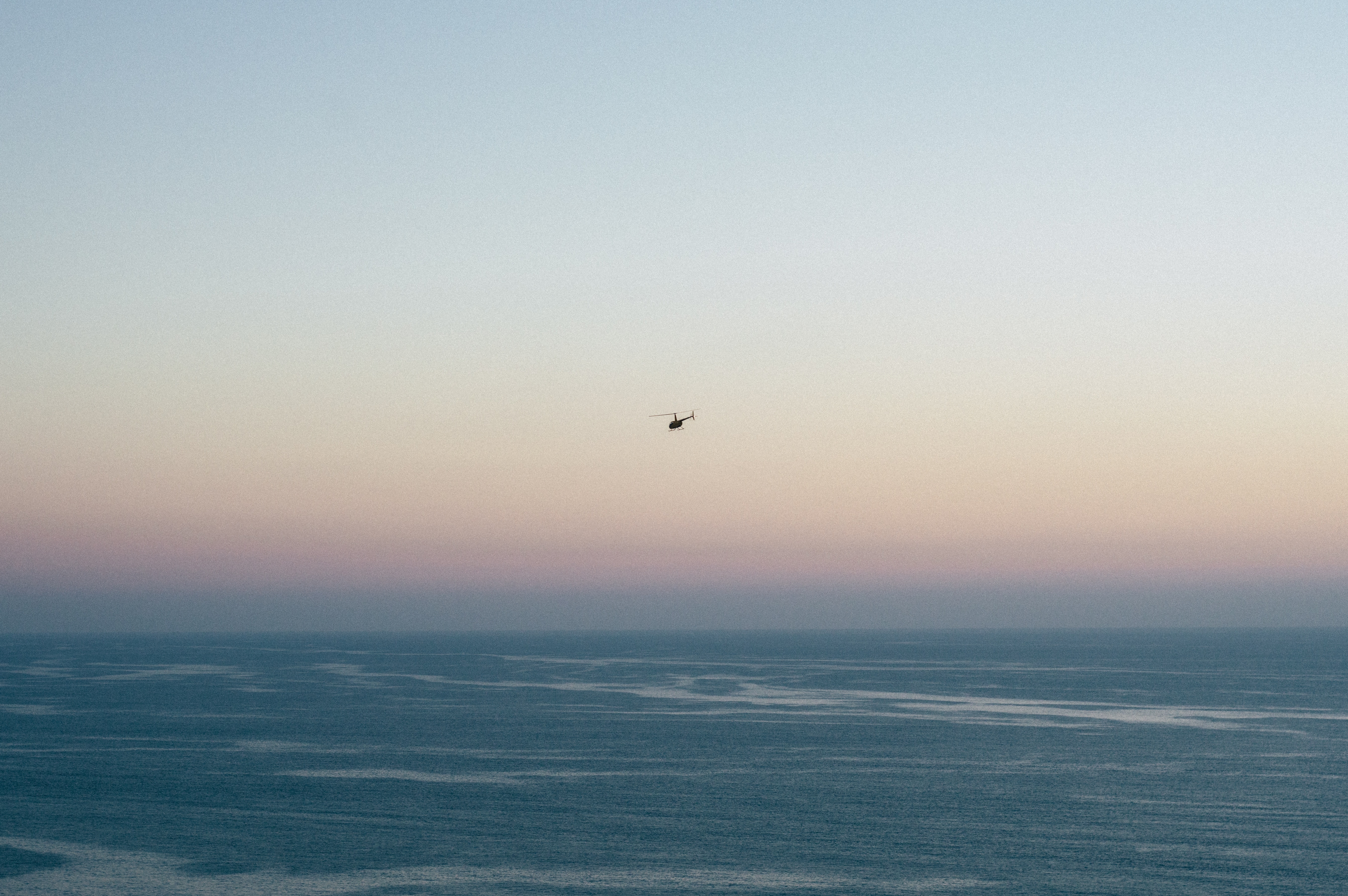 Helicopter flying over the ocean at sunset HD Wallpaper
