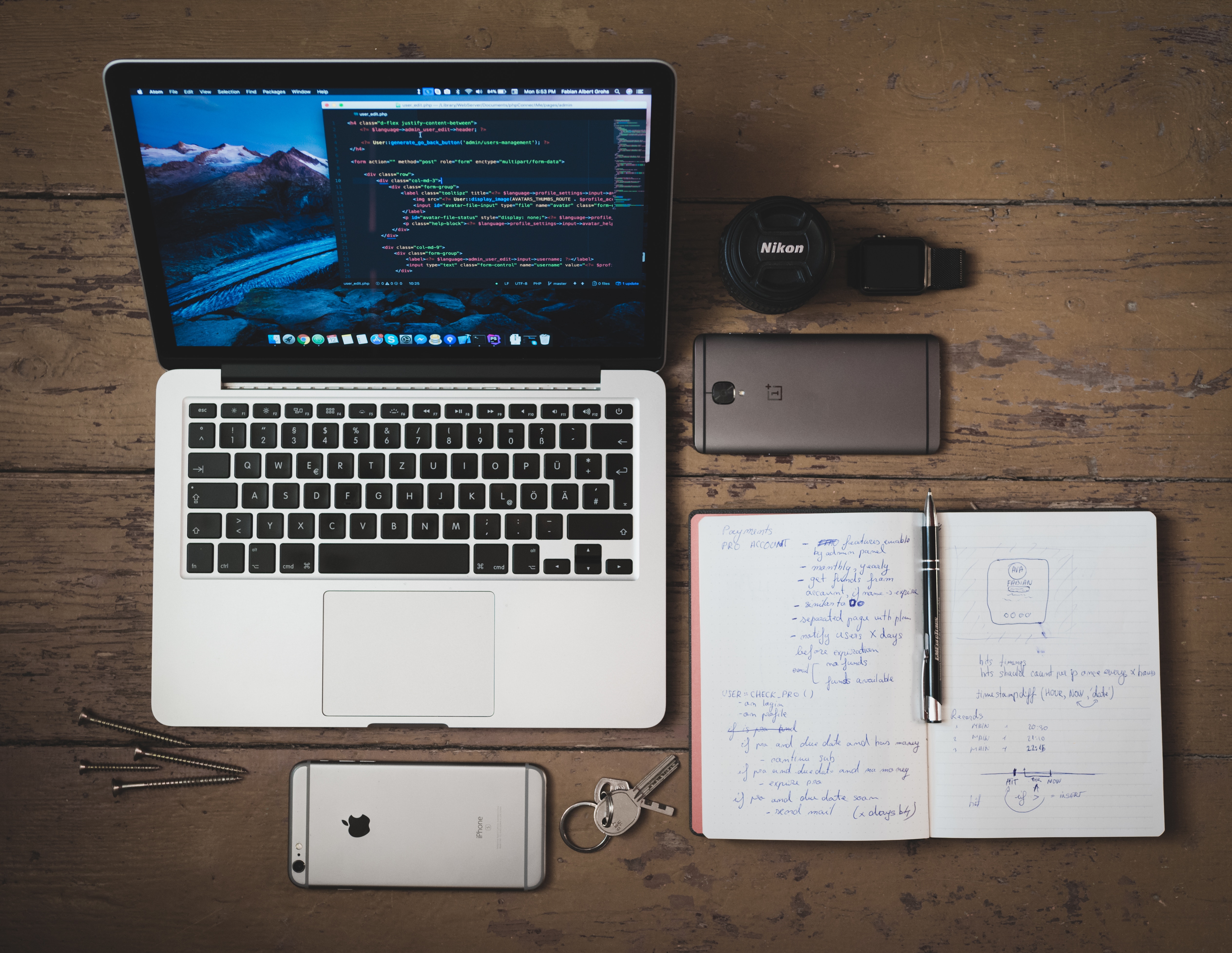 Laptop, phone, camera lens, notebook, and keys on a wooden desk HD Wallpaper