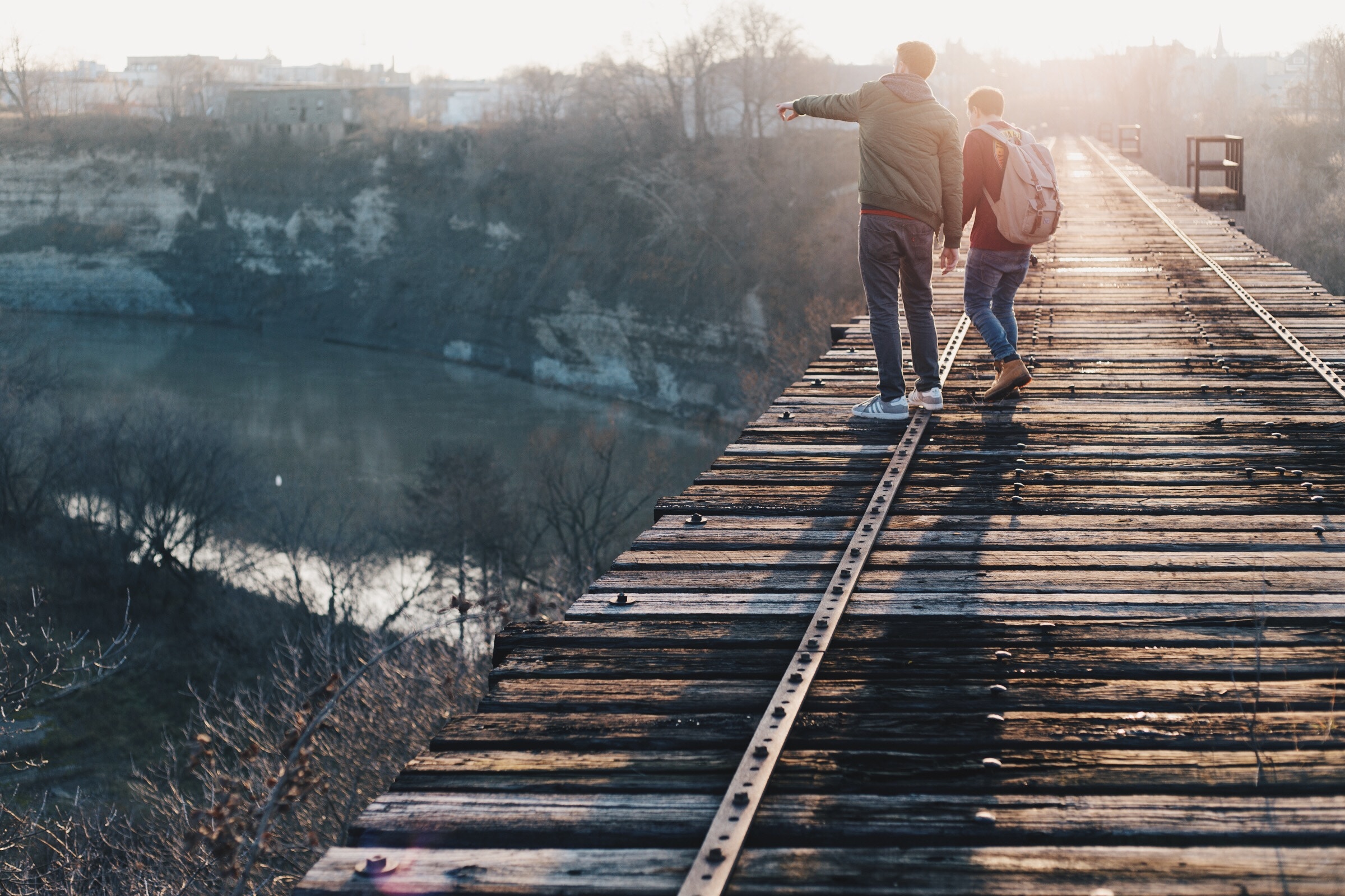 Two people on a wooden railway bridge at sunset HD Wallpaper