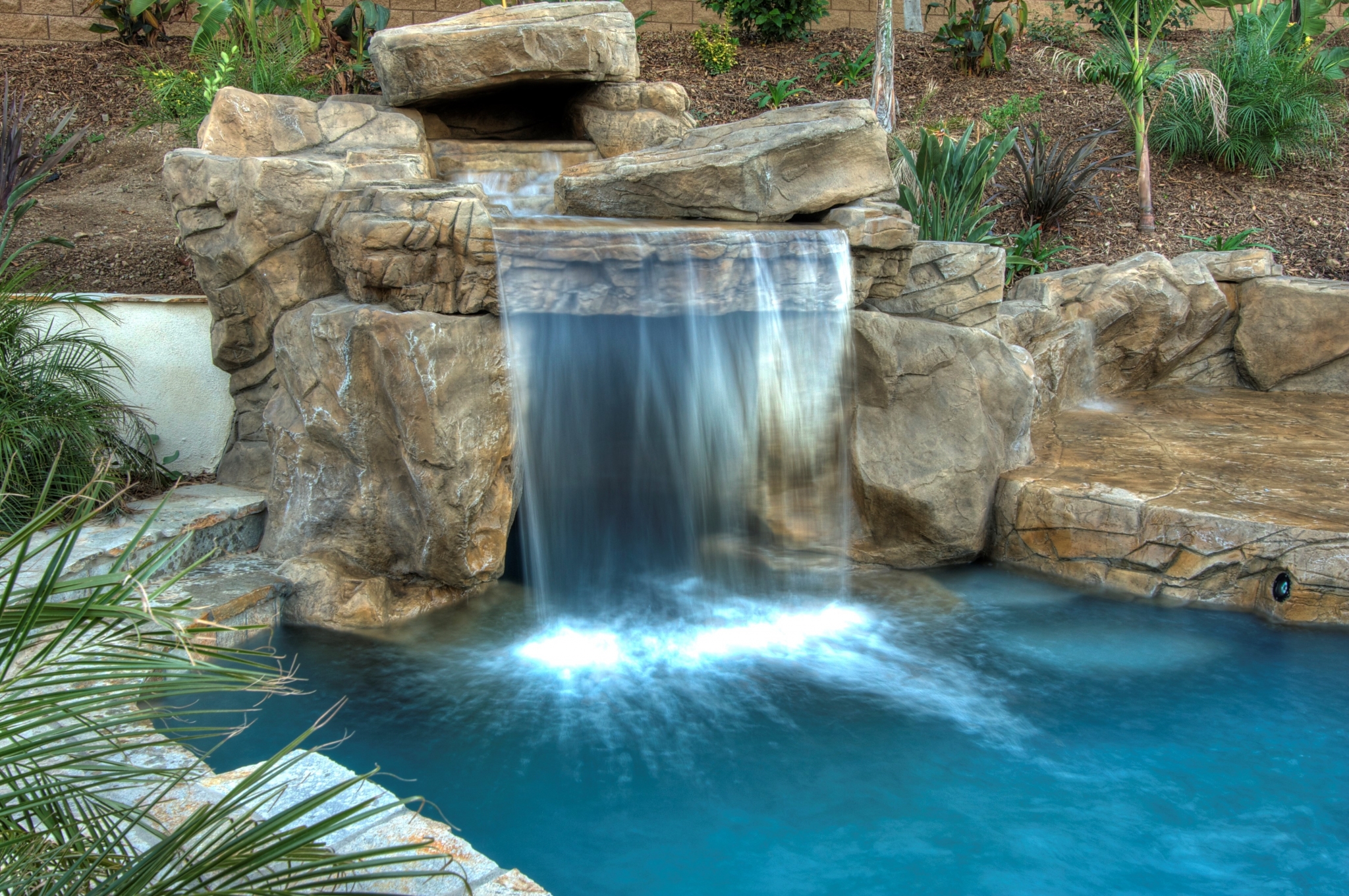 Artificial waterfall cascading into a swimming pool HD Wallpaper