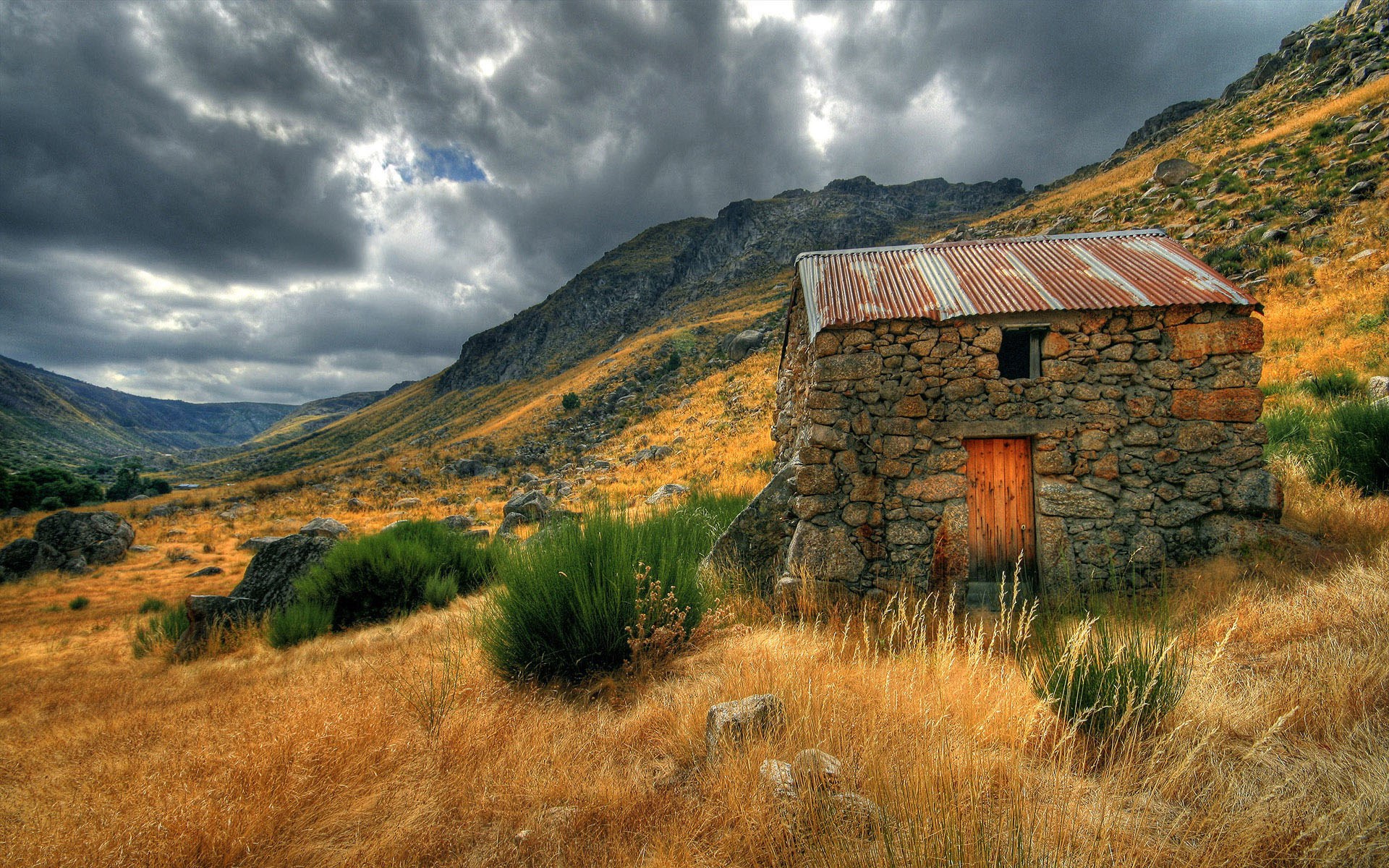 Stone cabin in a mountainous valley under stormy skies HD Wallpaper