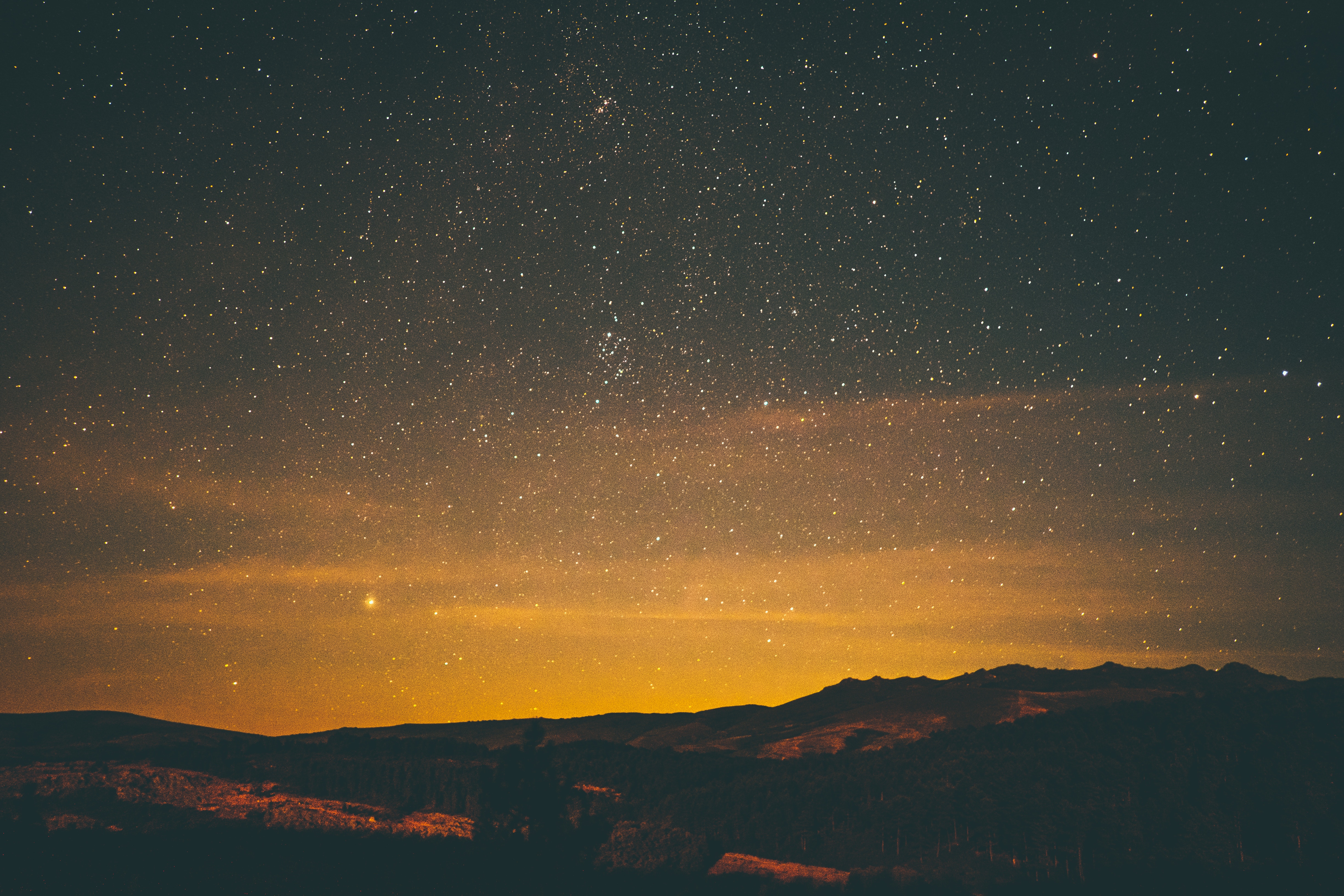 Starry night sky over mountains with orange glow HD Wallpaper