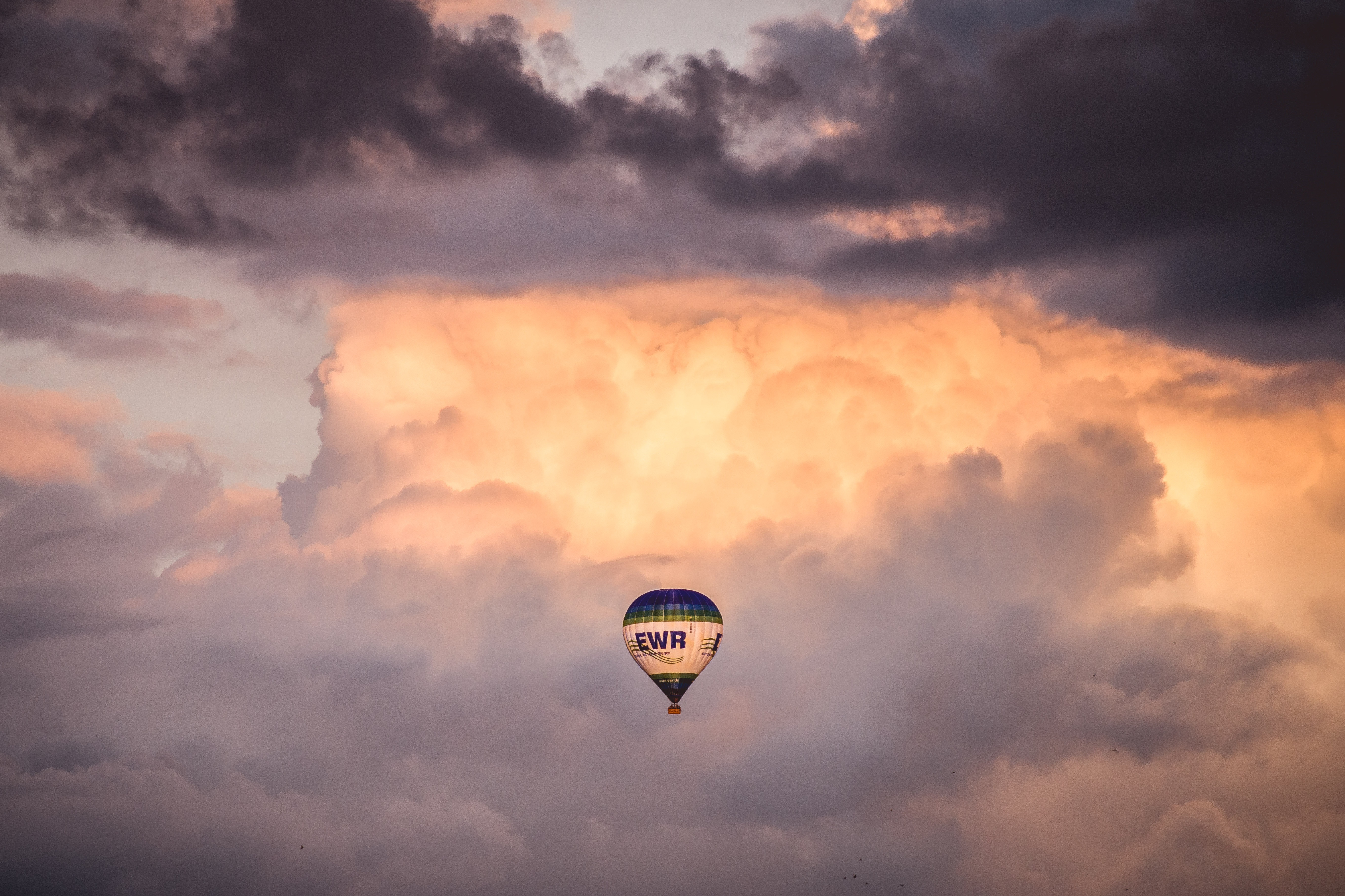 Hot air balloon floats among dramatic clouds at sunset HD Wallpaper