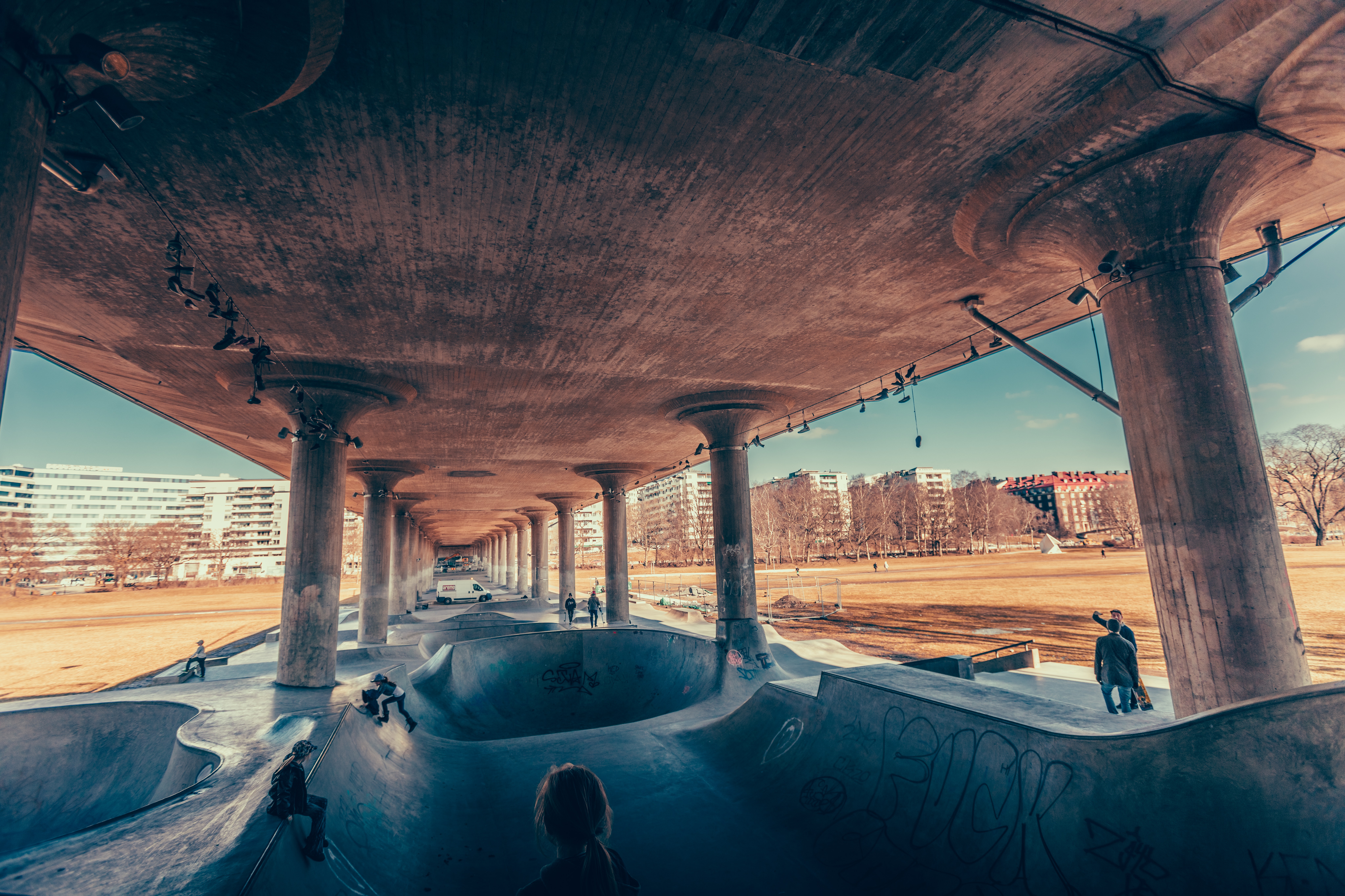 Skatepark under a concrete bridge with people skateboarding HD Wallpaper