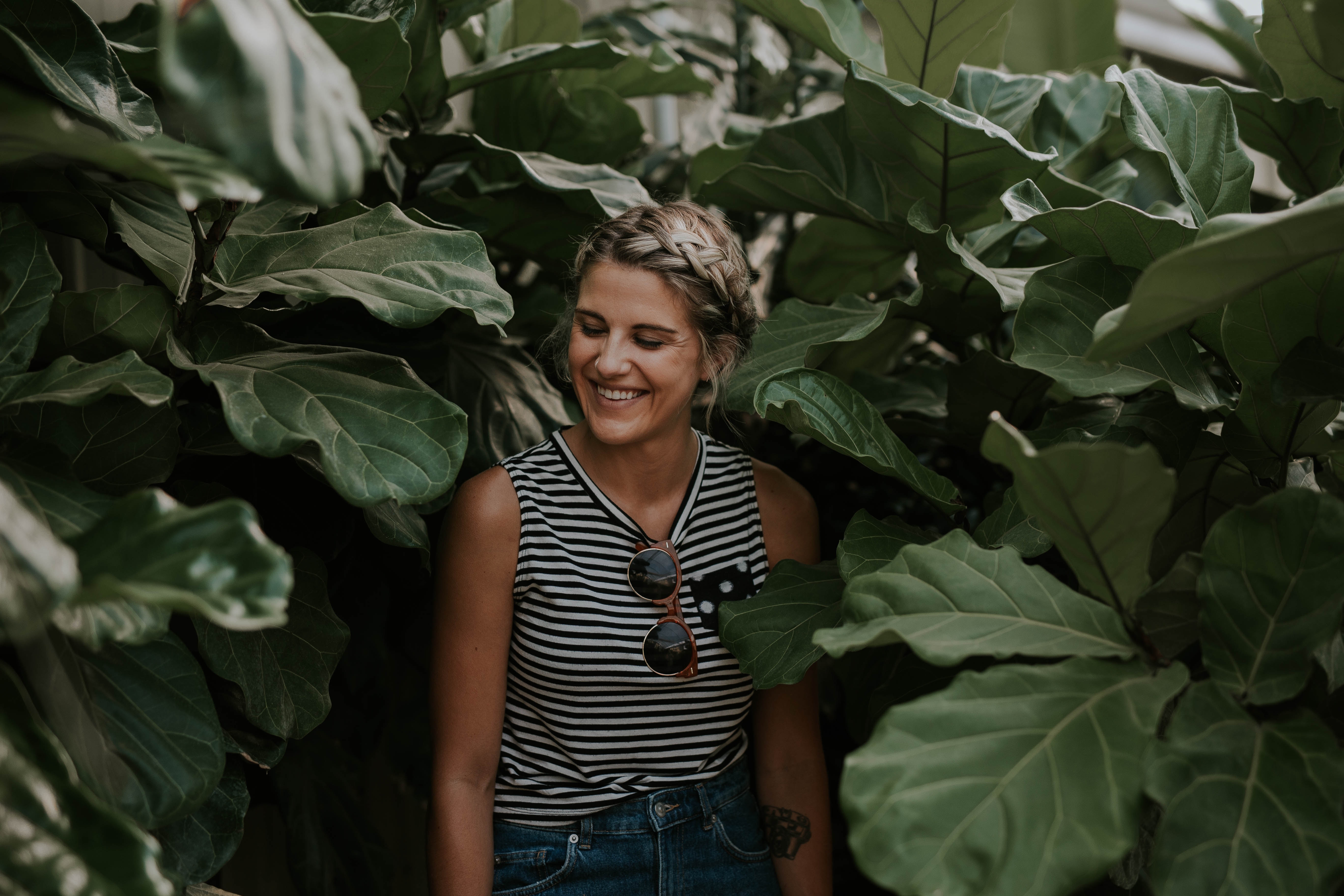 Woman with braided hair smiling among large green leaves HD Wallpaper
