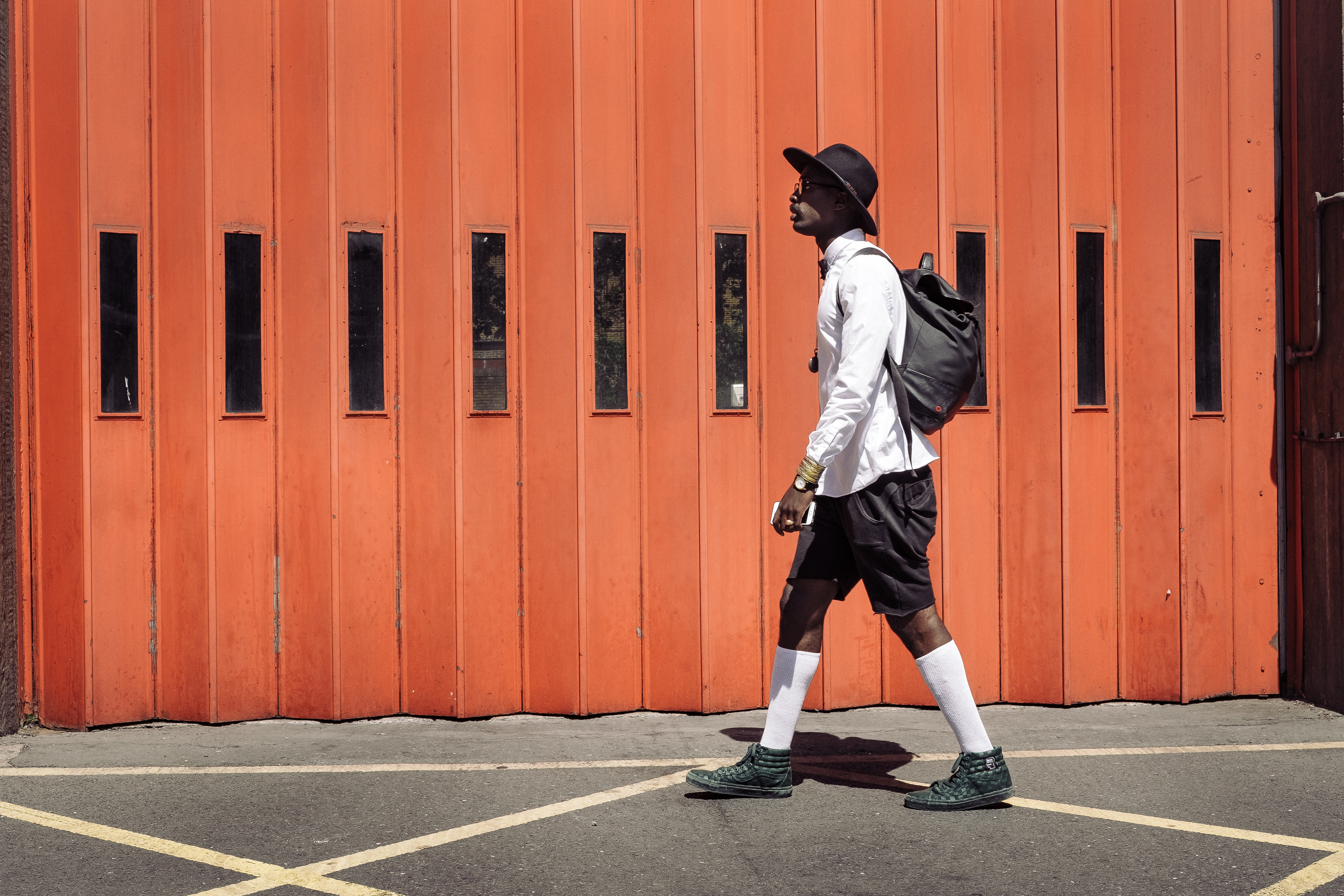 Man in hat and backpack walks by orange door HD Wallpaper