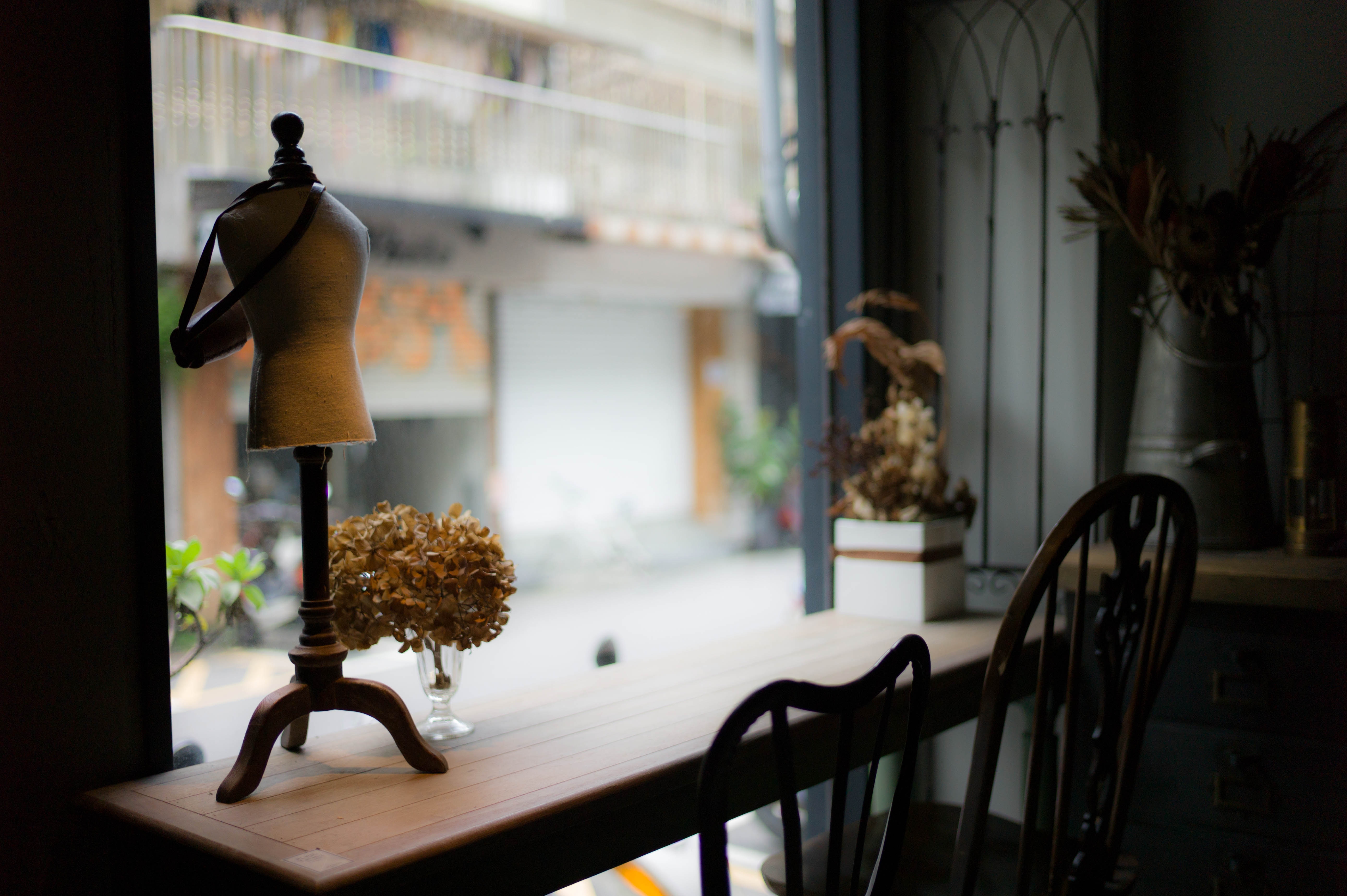 Miniature dress form and dried flowers on a table by the window HD Wallpaper