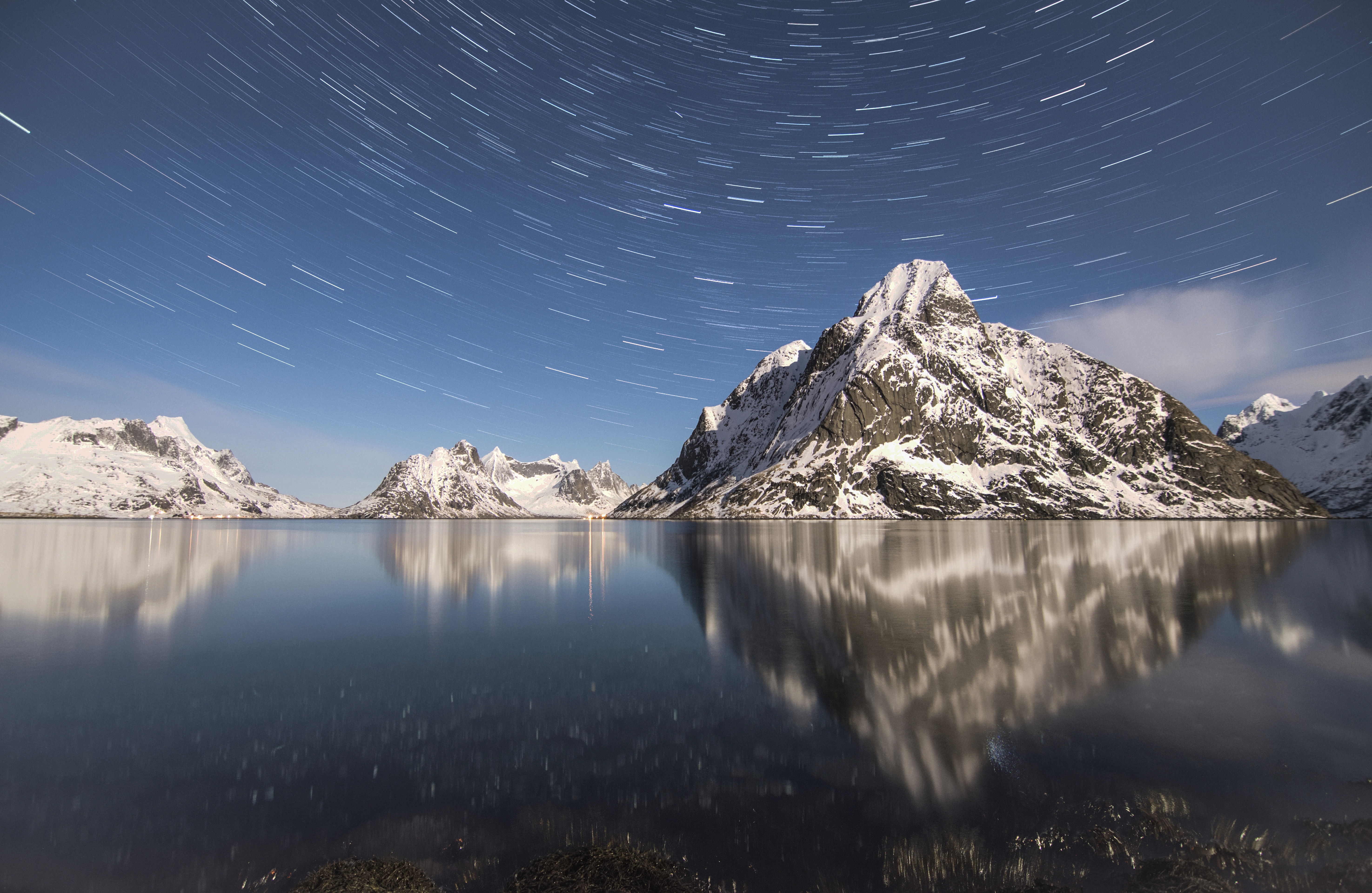 Snowy mountains reflected in a lake under a star trail sky HD Wallpaper
