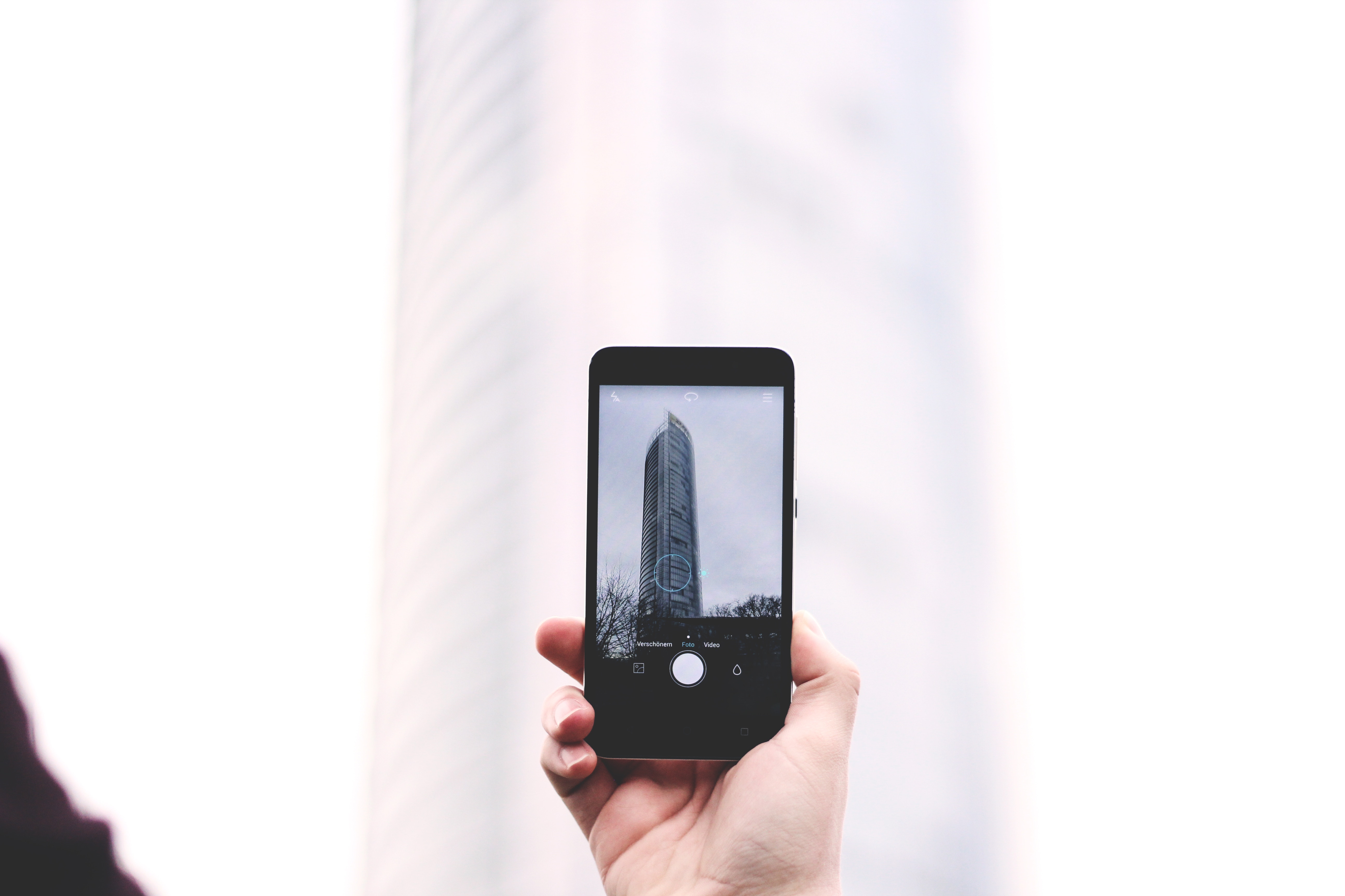 Hand holding iPhone taking a photo of a skyscraper HD Wallpaper