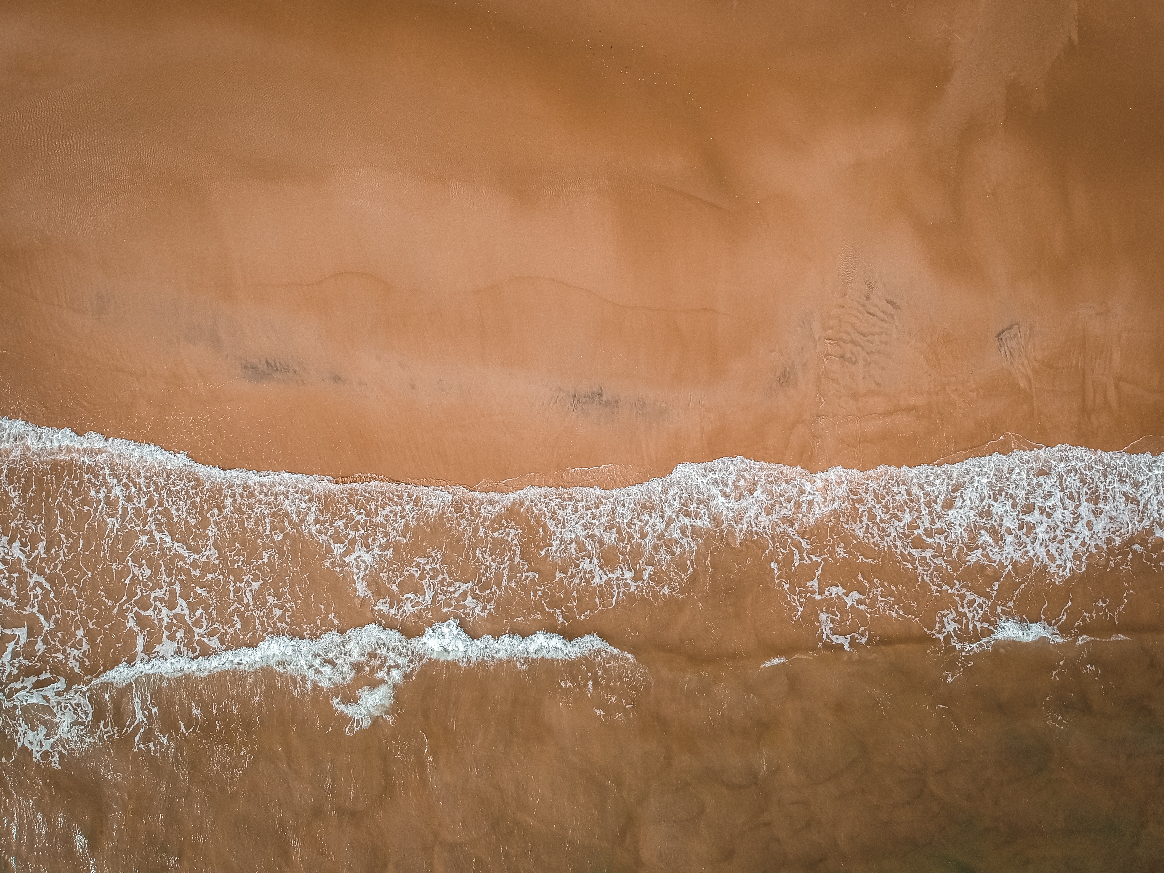 Aerial view of waves crashing on a sandy beach in Uruguay HD Wallpaper