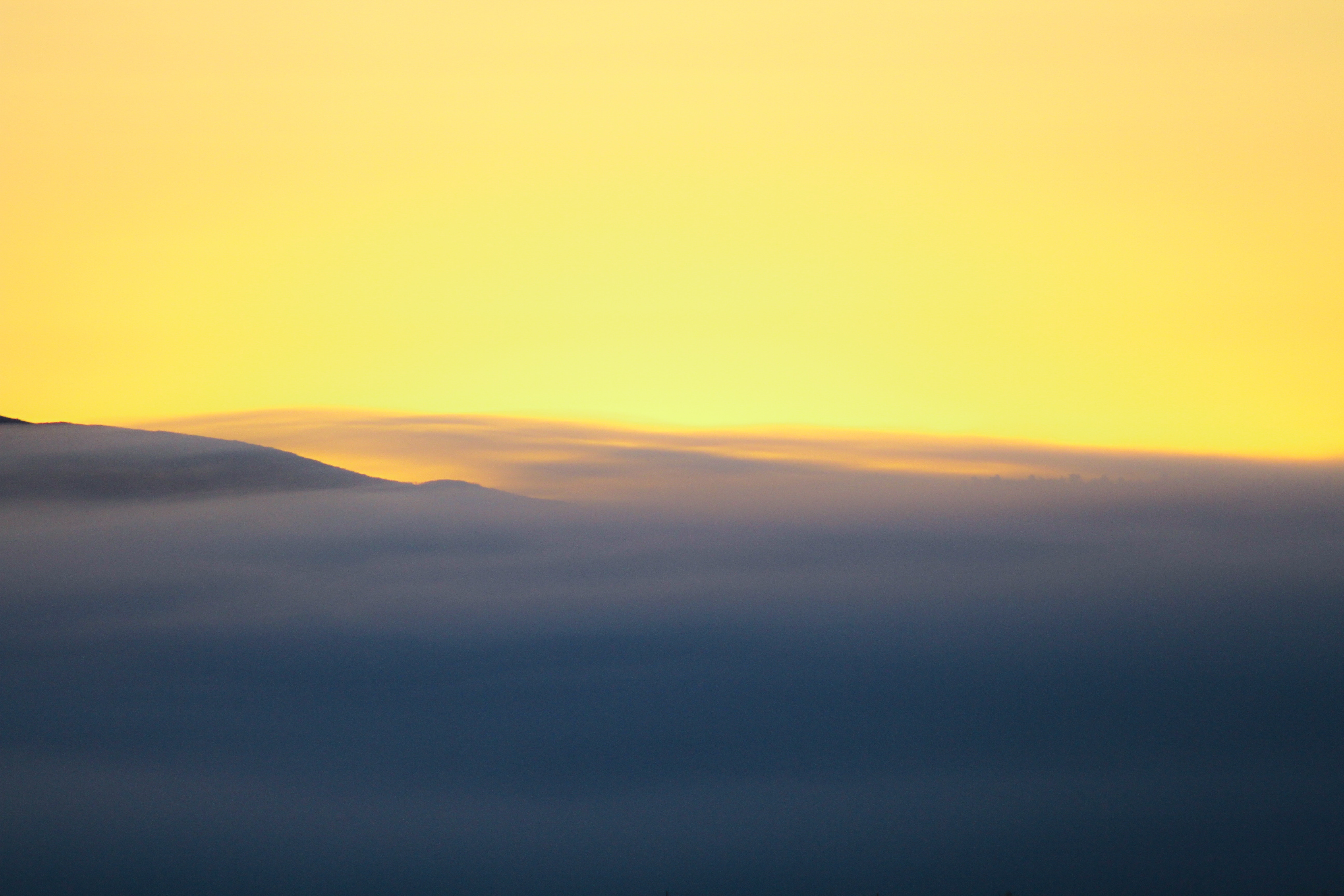 Mountain range covered in fog under a yellow sky HD Wallpaper