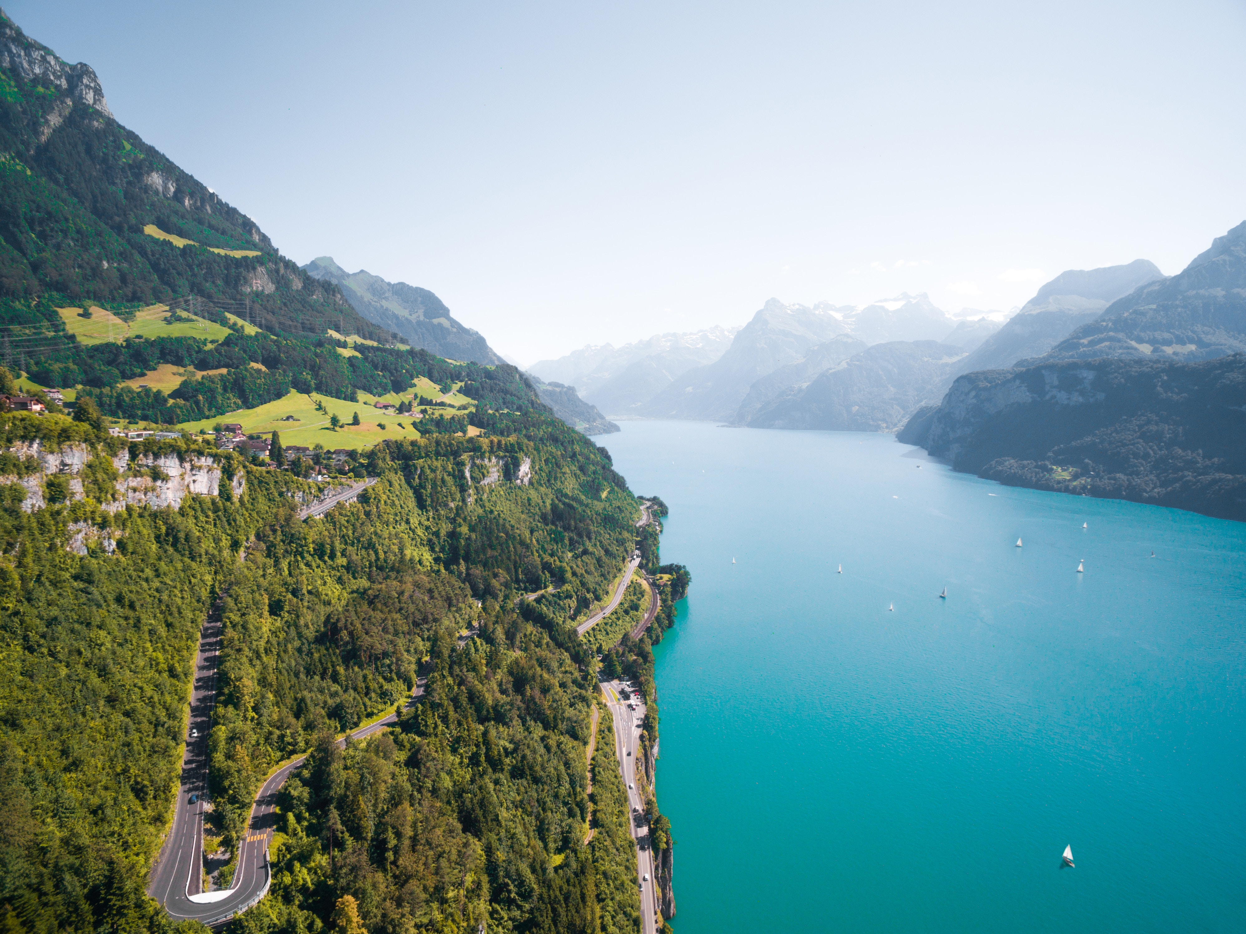 Winding road along a turquoise lake in the mountains HD Wallpaper