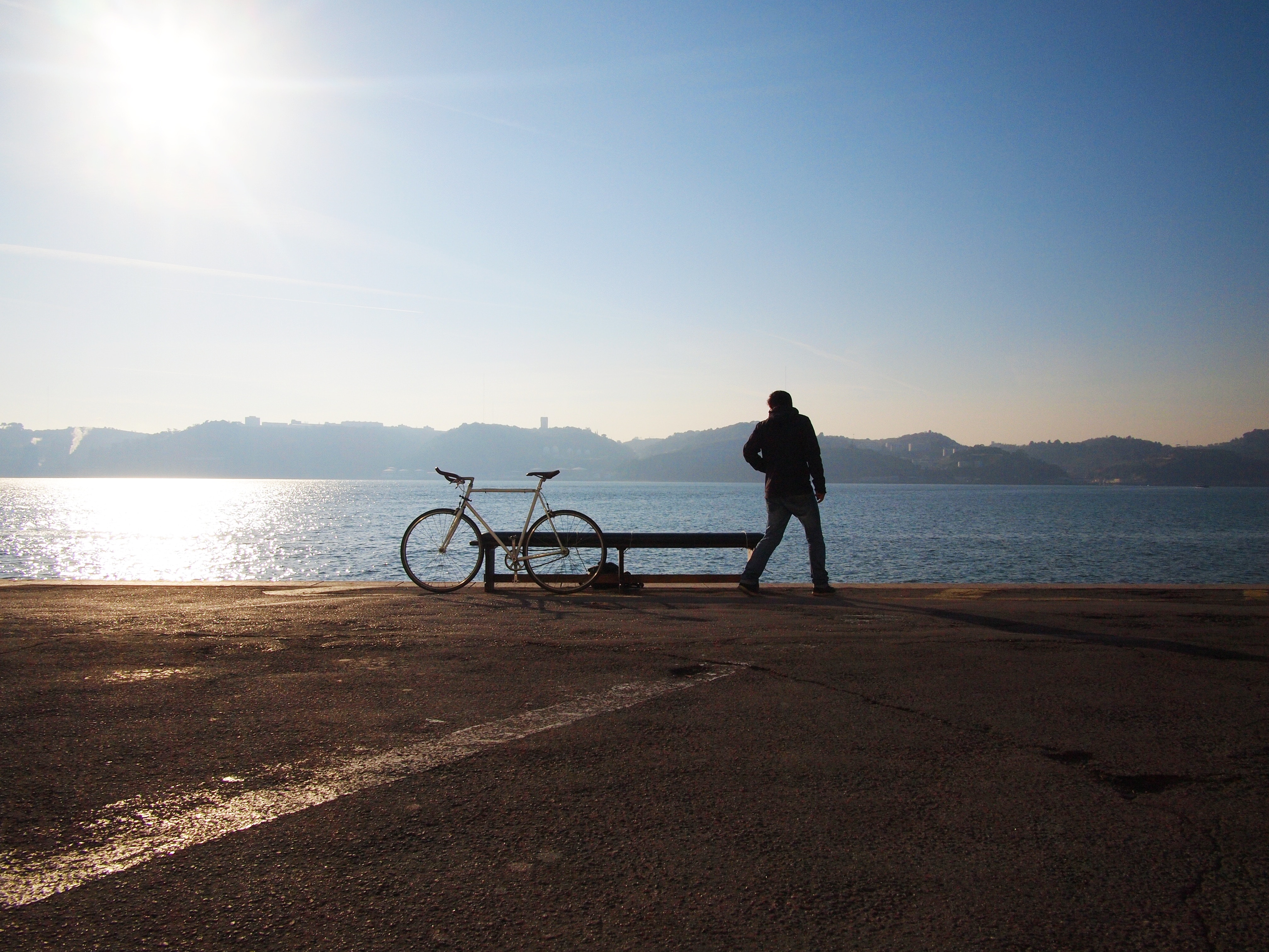 Man and bicycle on a waterfront with sun rays HD Wallpaper