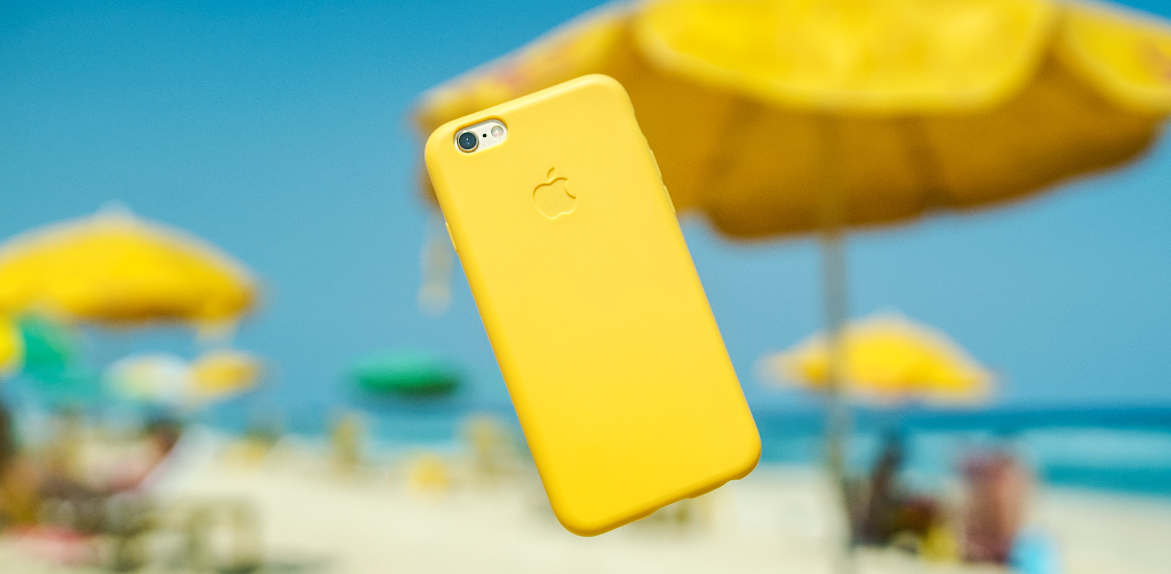 Yellow iPhone levitating on a beach with umbrellas HD Wallpaper