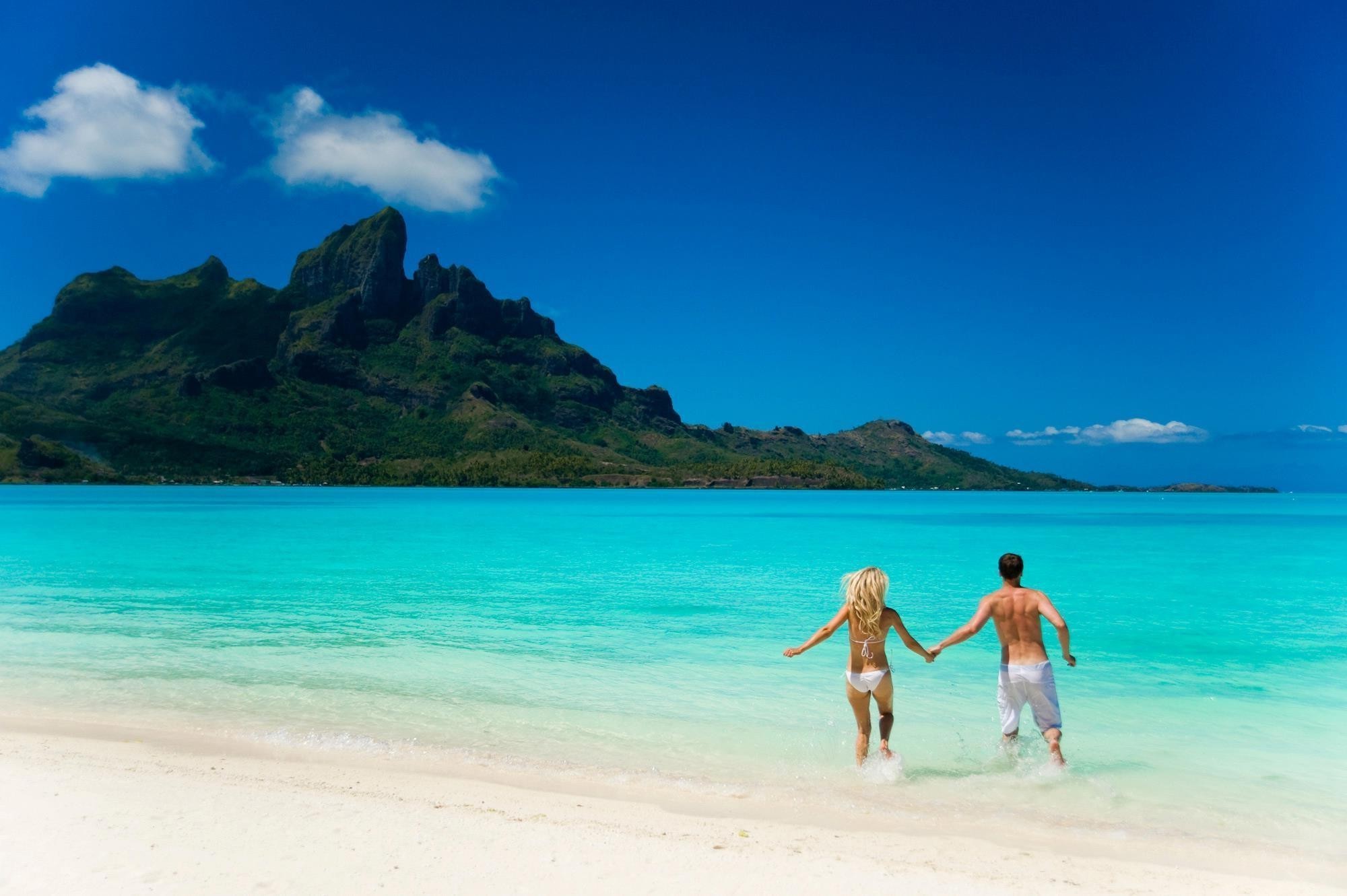 Couple Running into Turquoise Beach Water with Mountain View HD Wallpaper