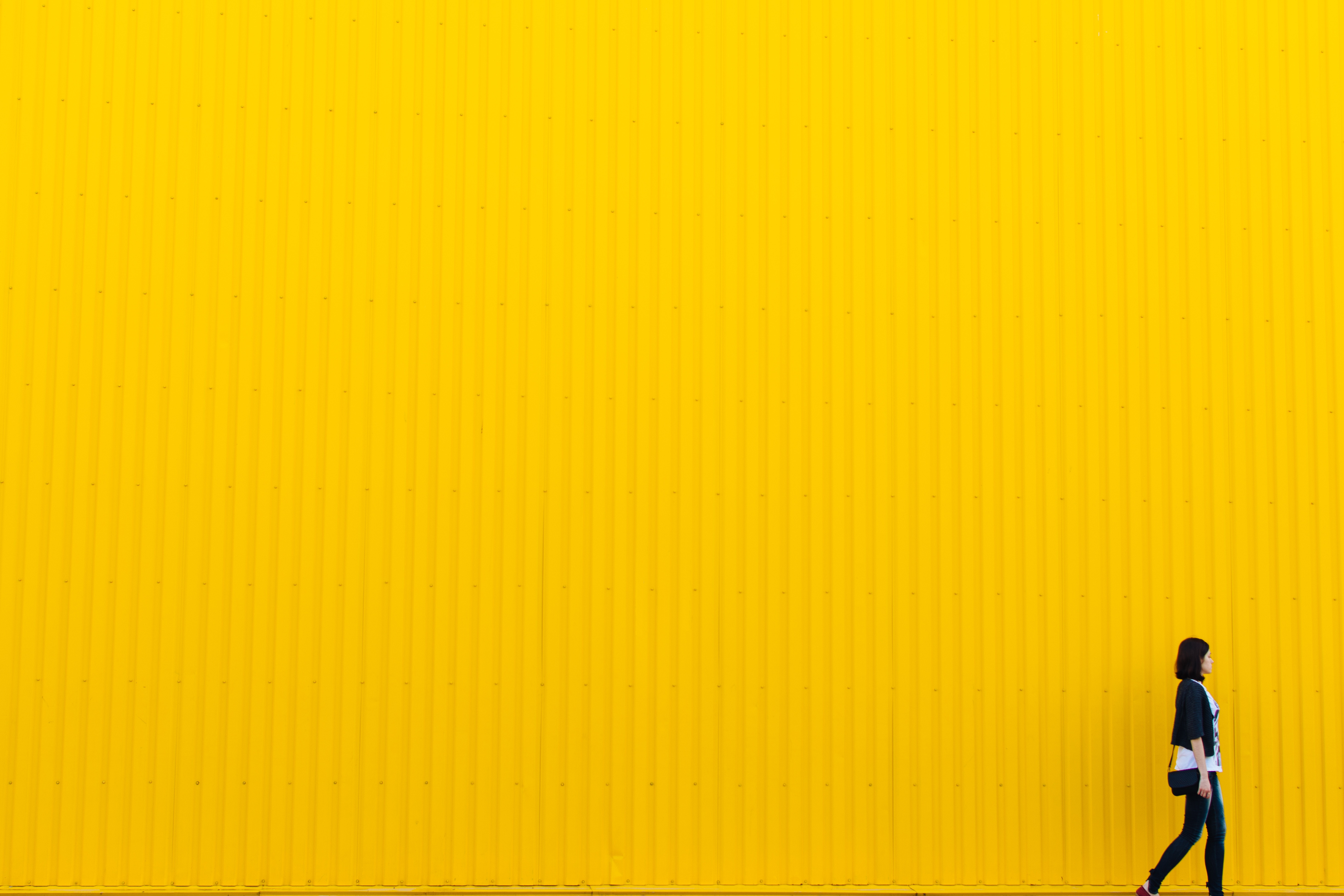 Woman walking in front of a yellow corrugated wall HD Wallpaper