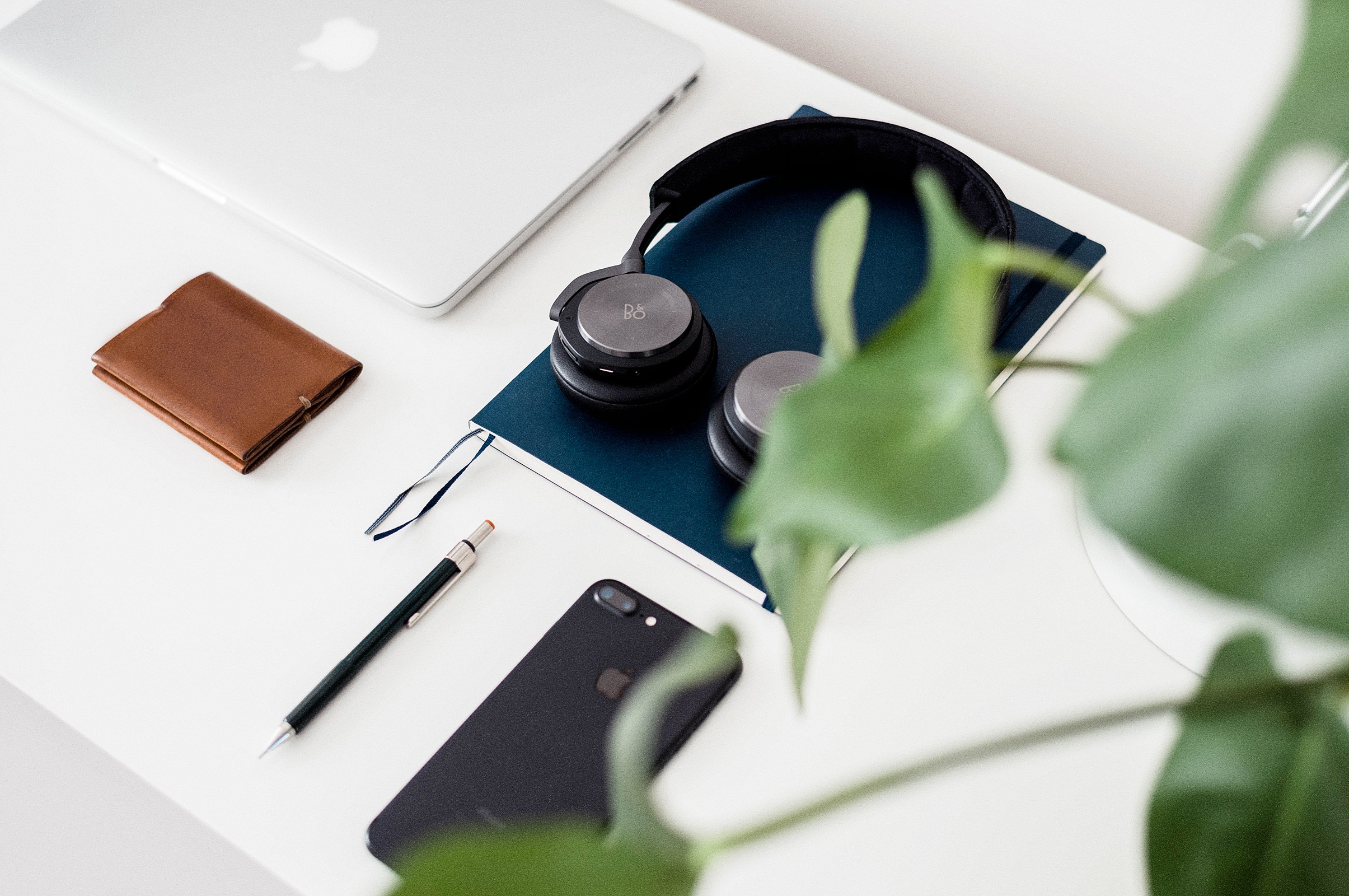 Apple Laptop, Headphones, Wallet, Phone, and Plant on Desk HD Wallpaper