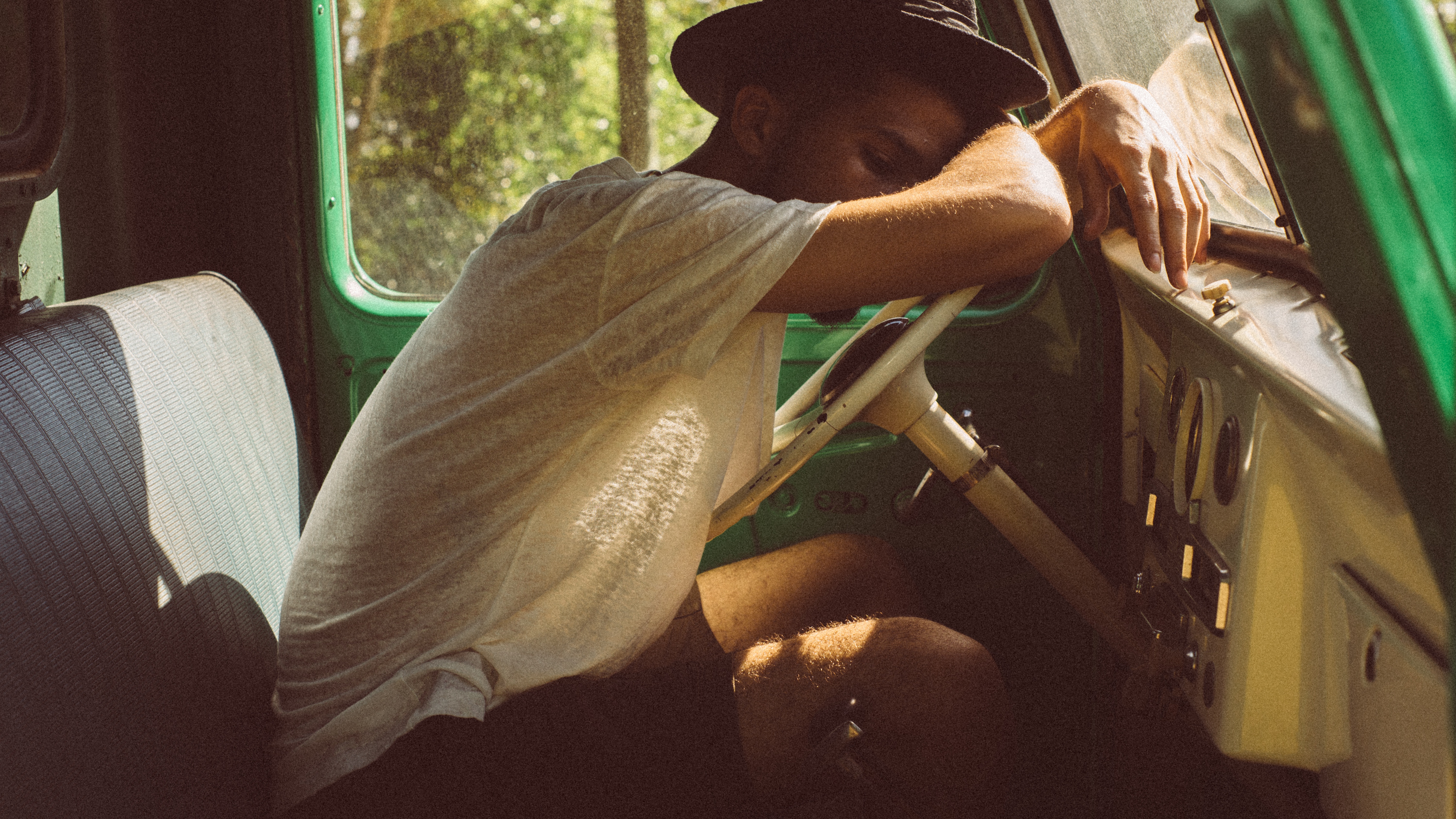 Man in hat sleeping in old green car HD Wallpaper