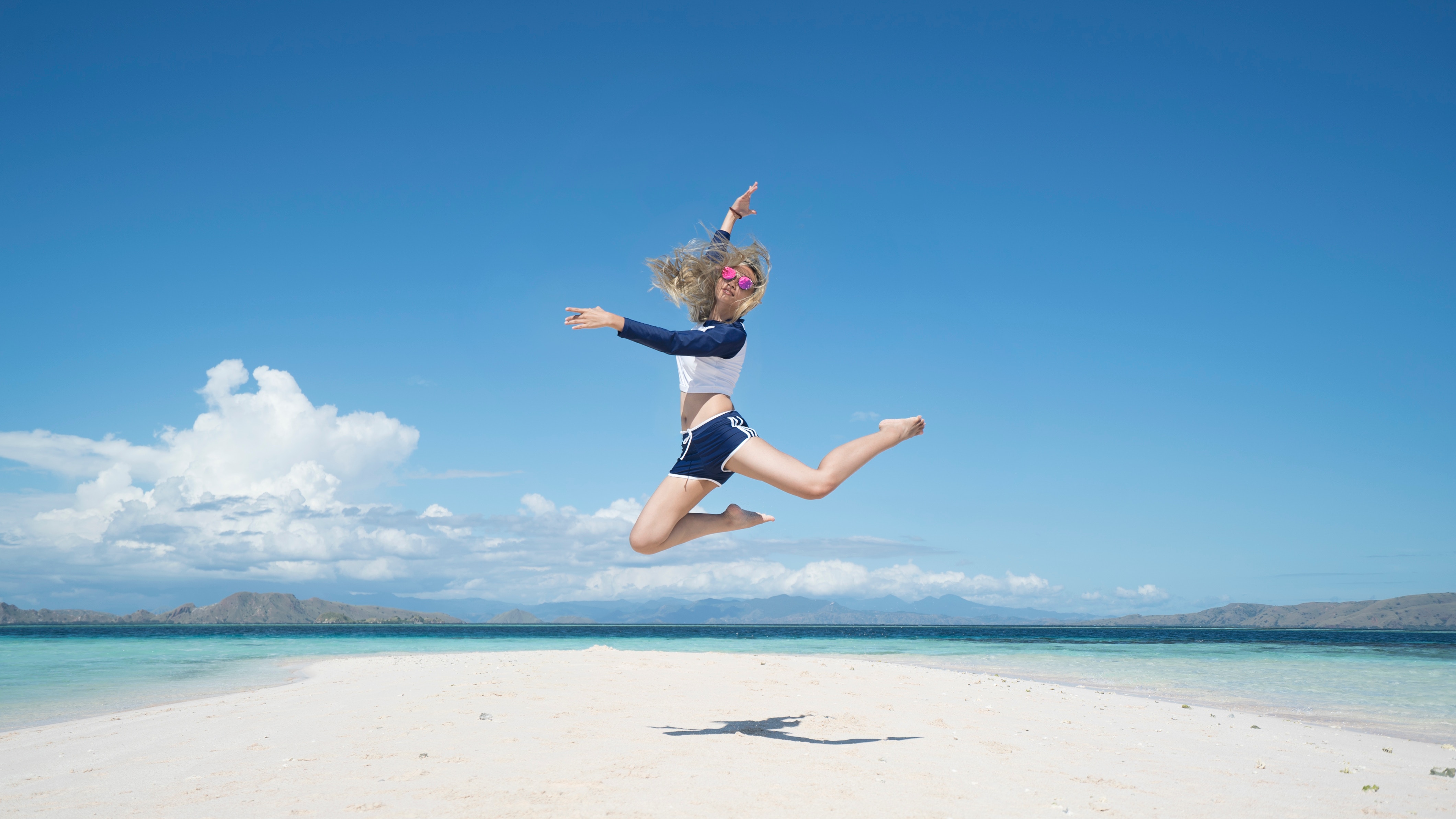 Woman jumping on a beach with blue sky and ocean HD Wallpaper