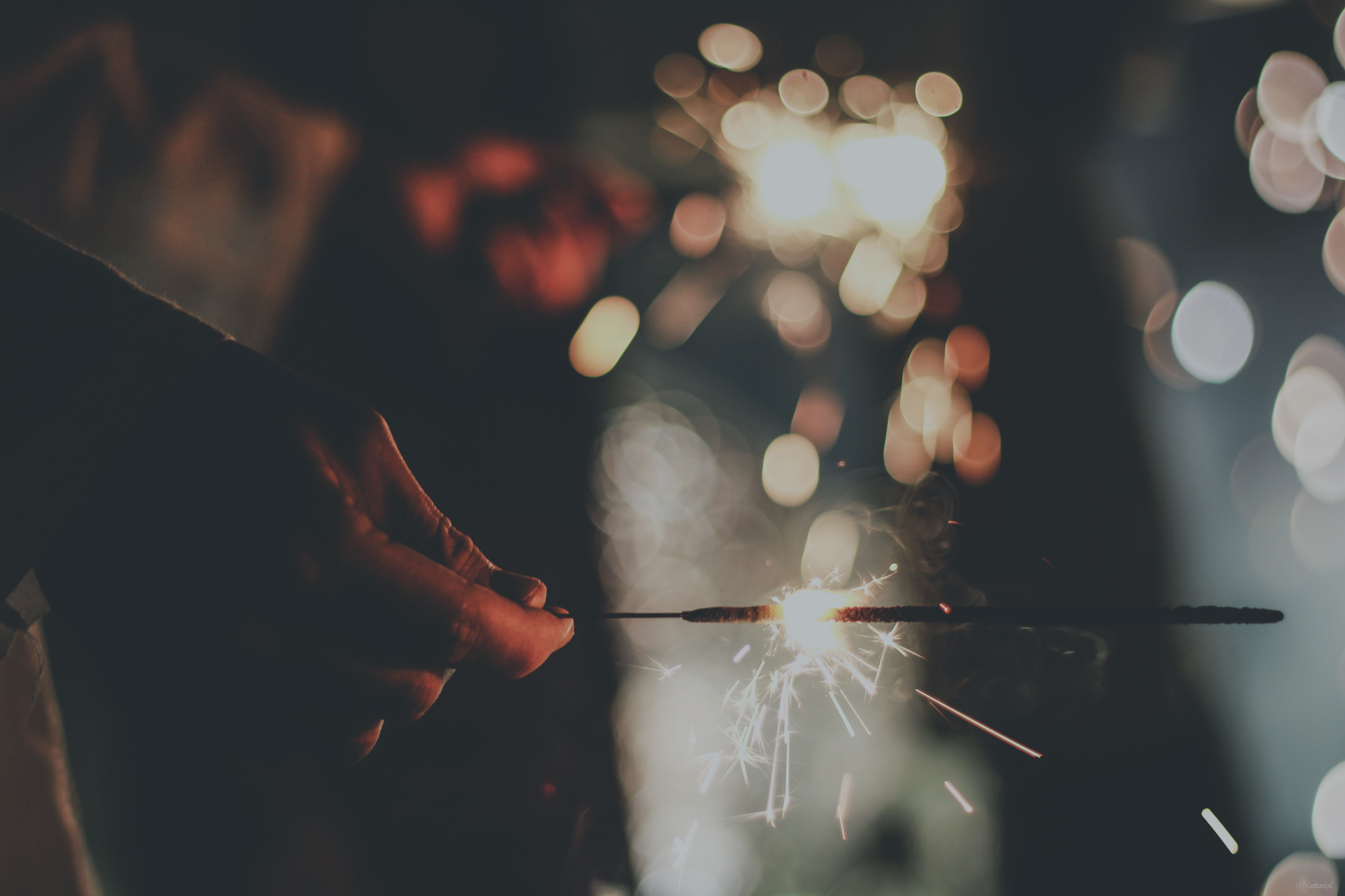 Person holding a sparkler at night with bokeh lights HD Wallpaper