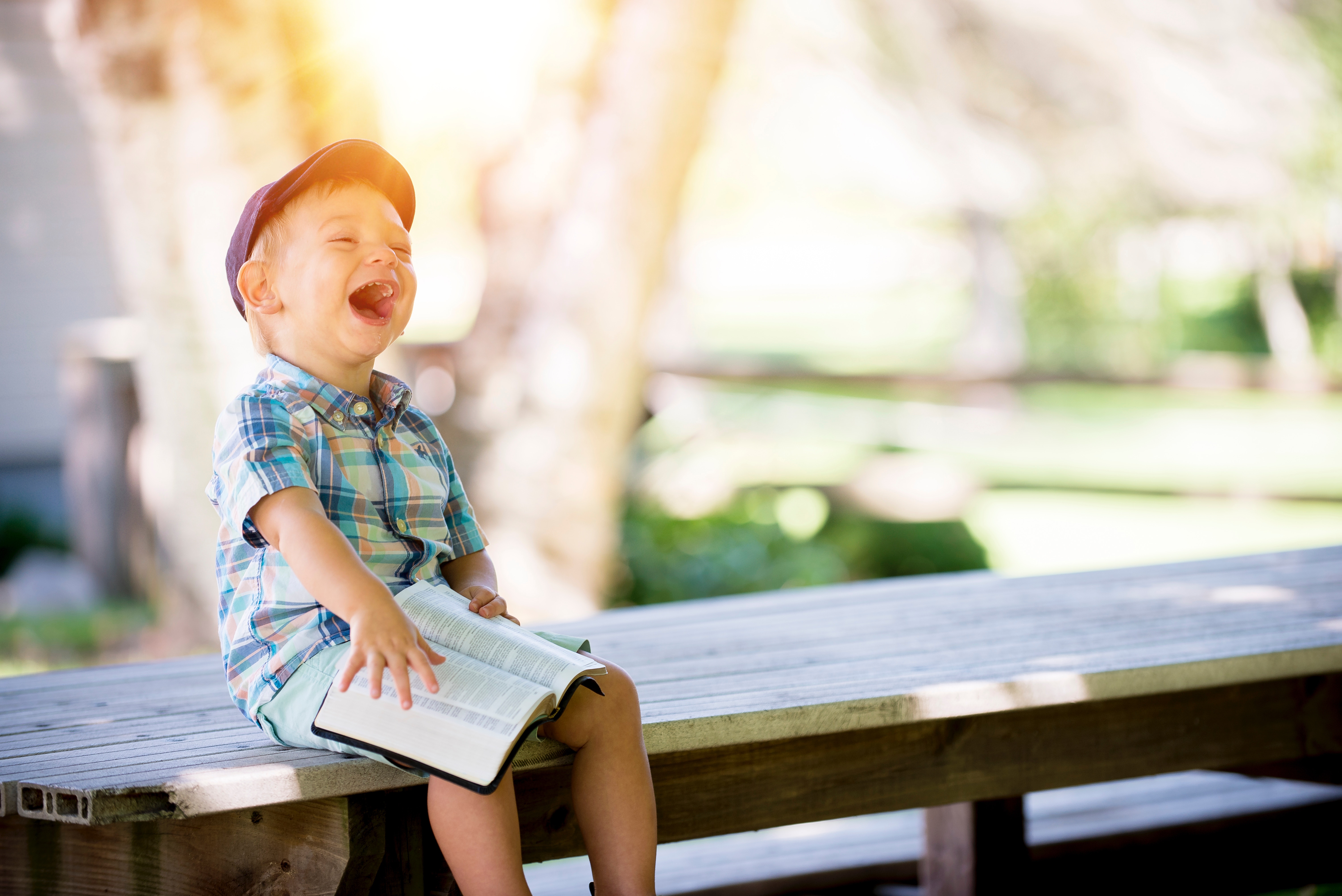 Boy in plaid shirt laughing with a book HD Wallpaper