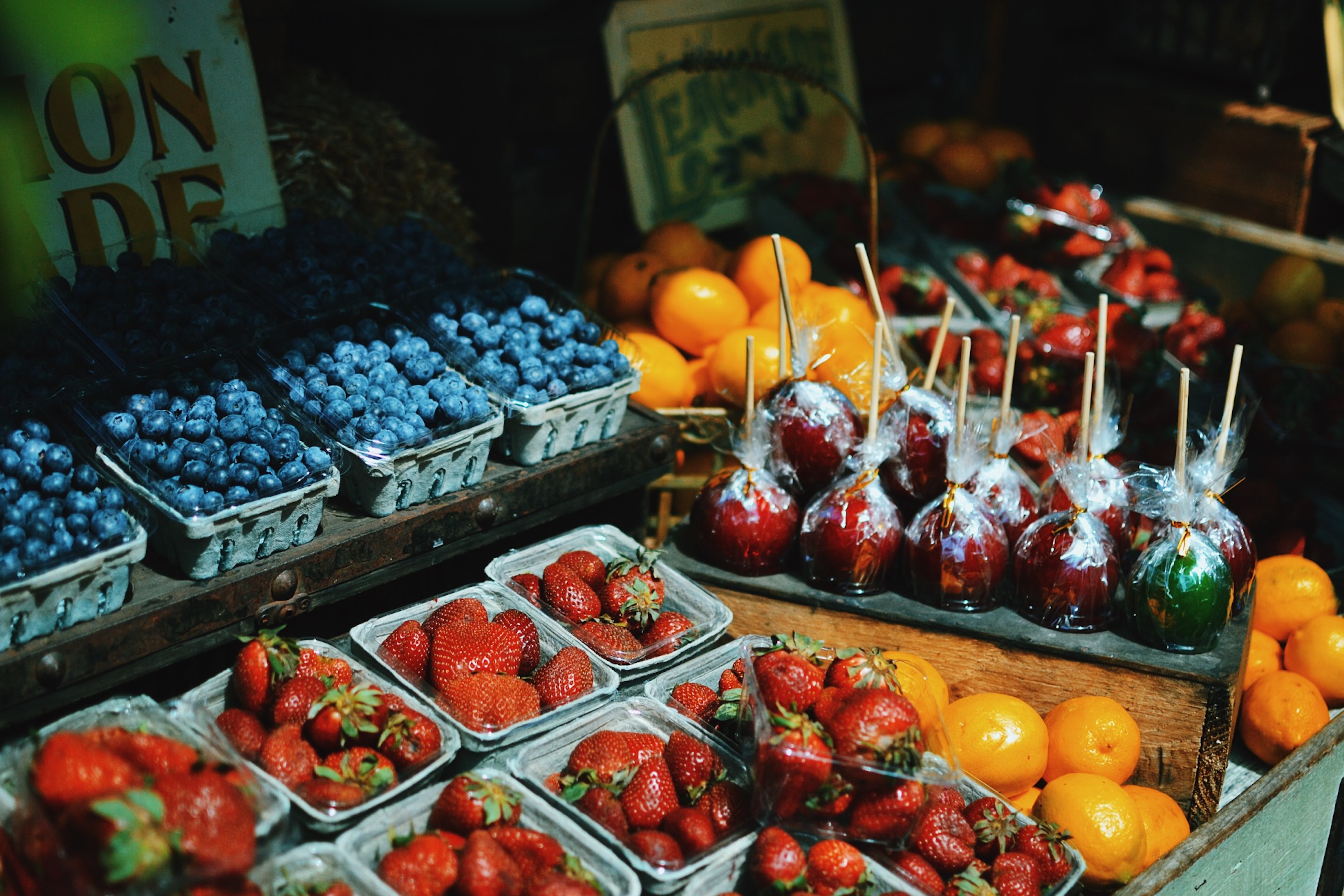 Fruit stall with blueberries, strawberries, oranges, and candy apples HD Wallpaper