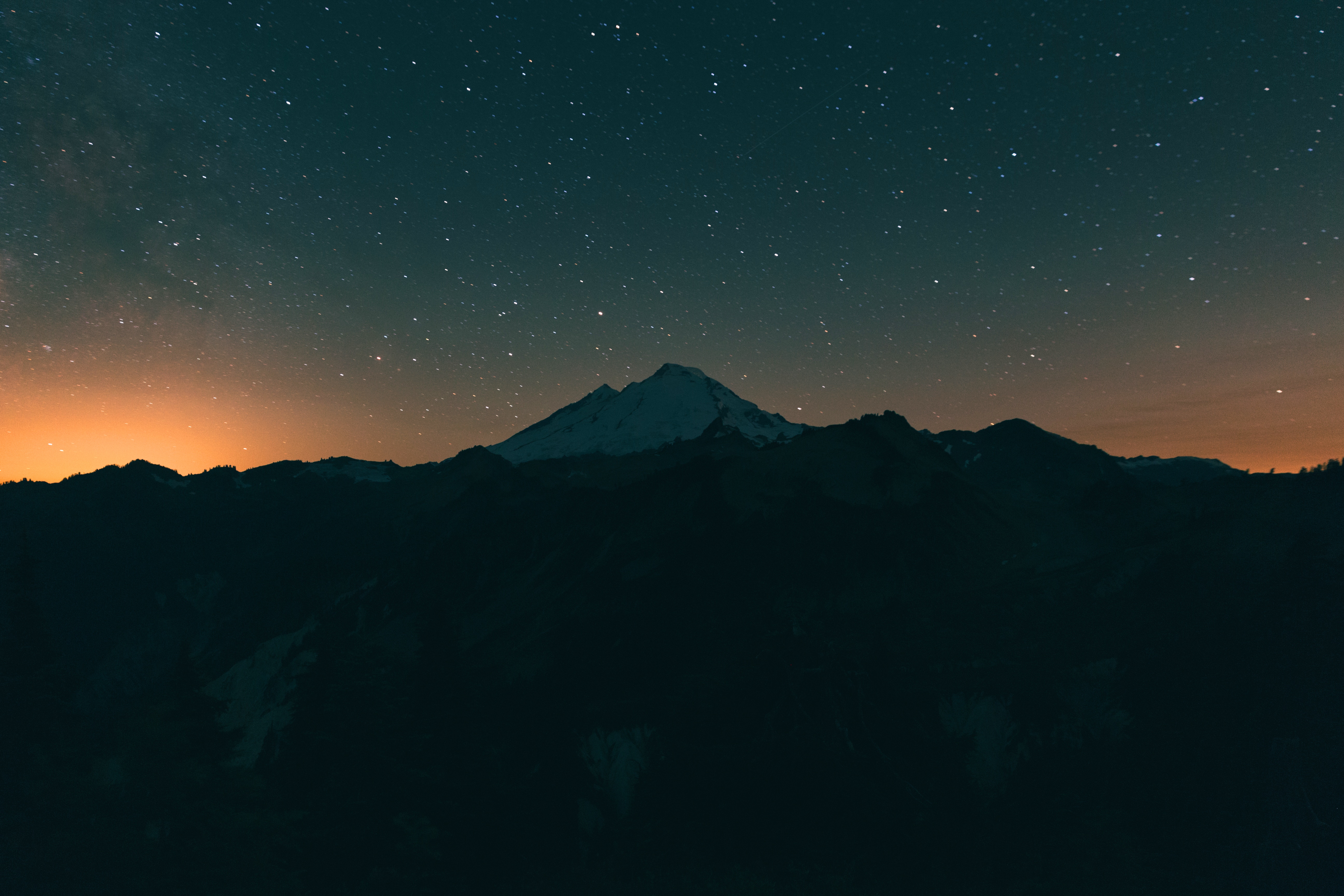 Mountain range under a starry night sky with orange glow HD Wallpaper