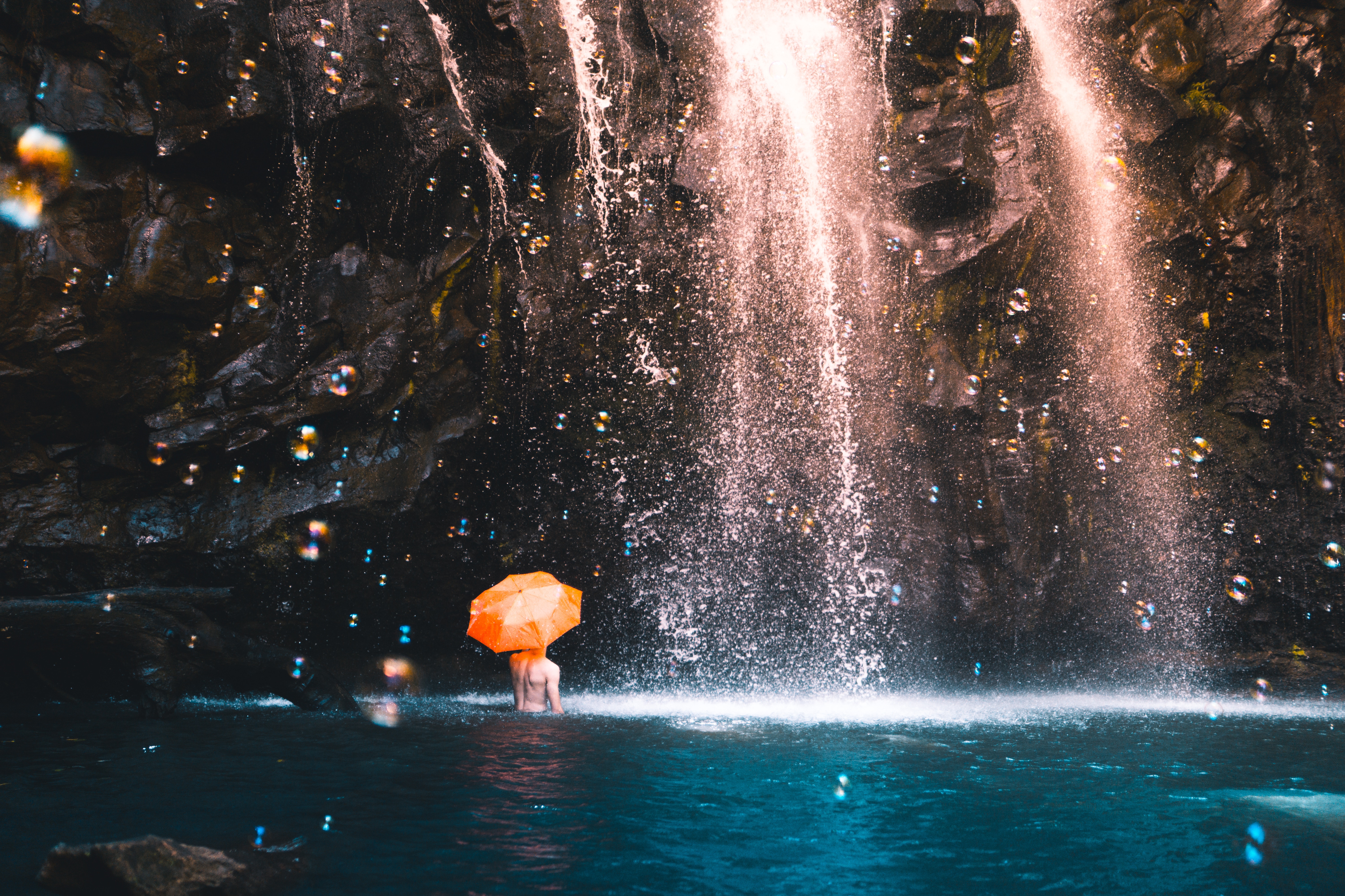 Person with orange umbrella under a waterfall HD Wallpaper