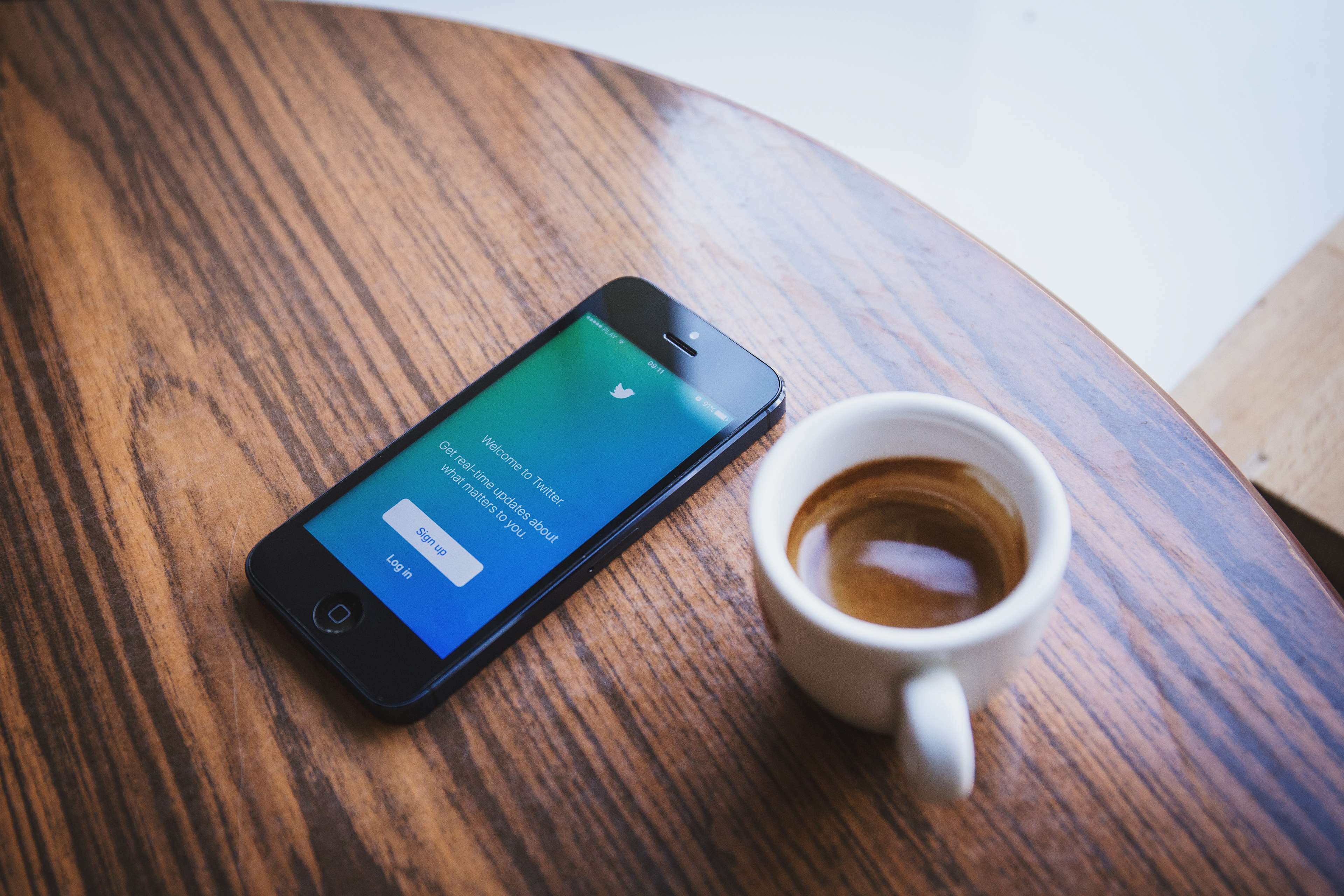 iPhone with Twitter app and coffee cup on wooden table HD Wallpaper
