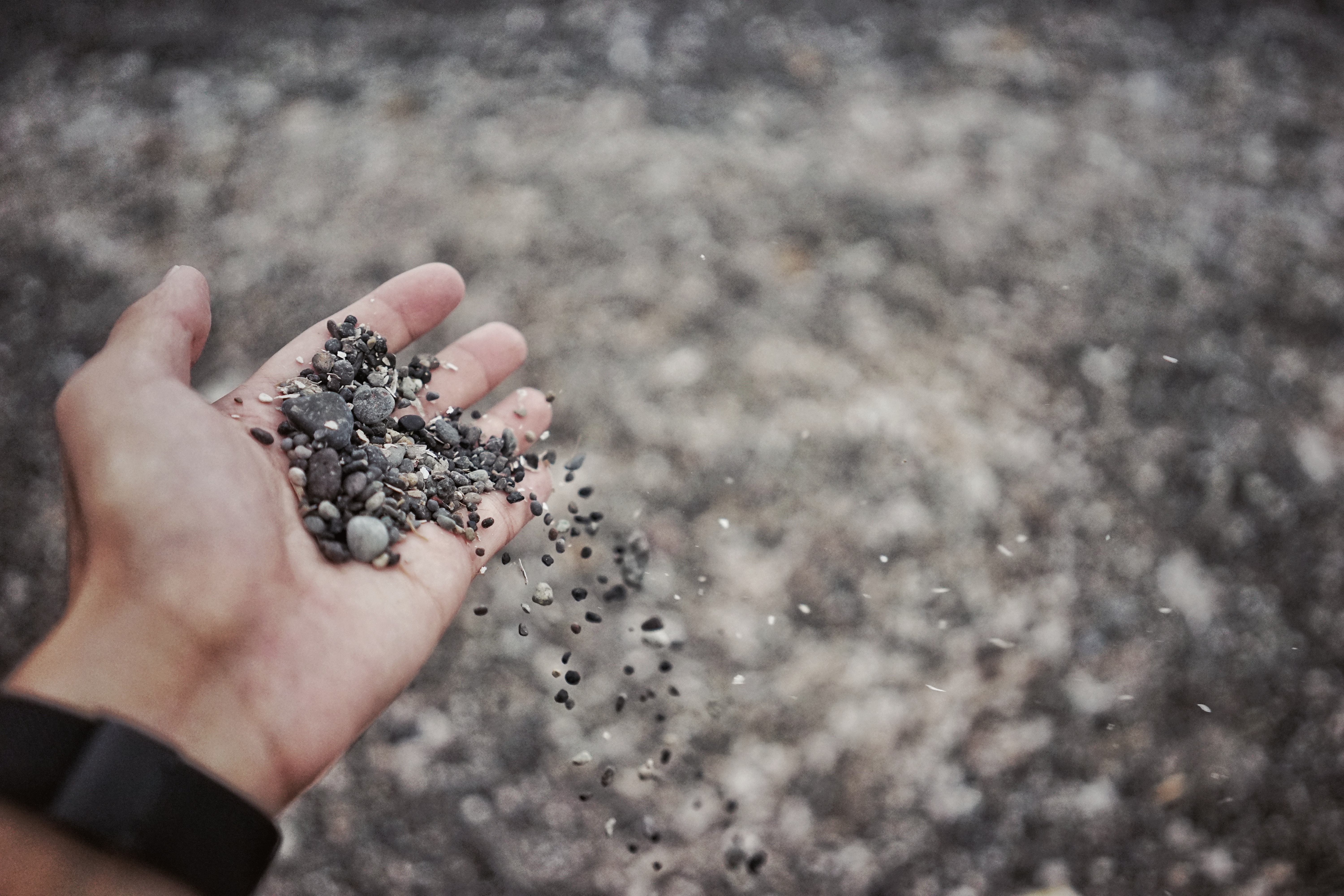 Hand holding and dropping small pebbles HD Wallpaper