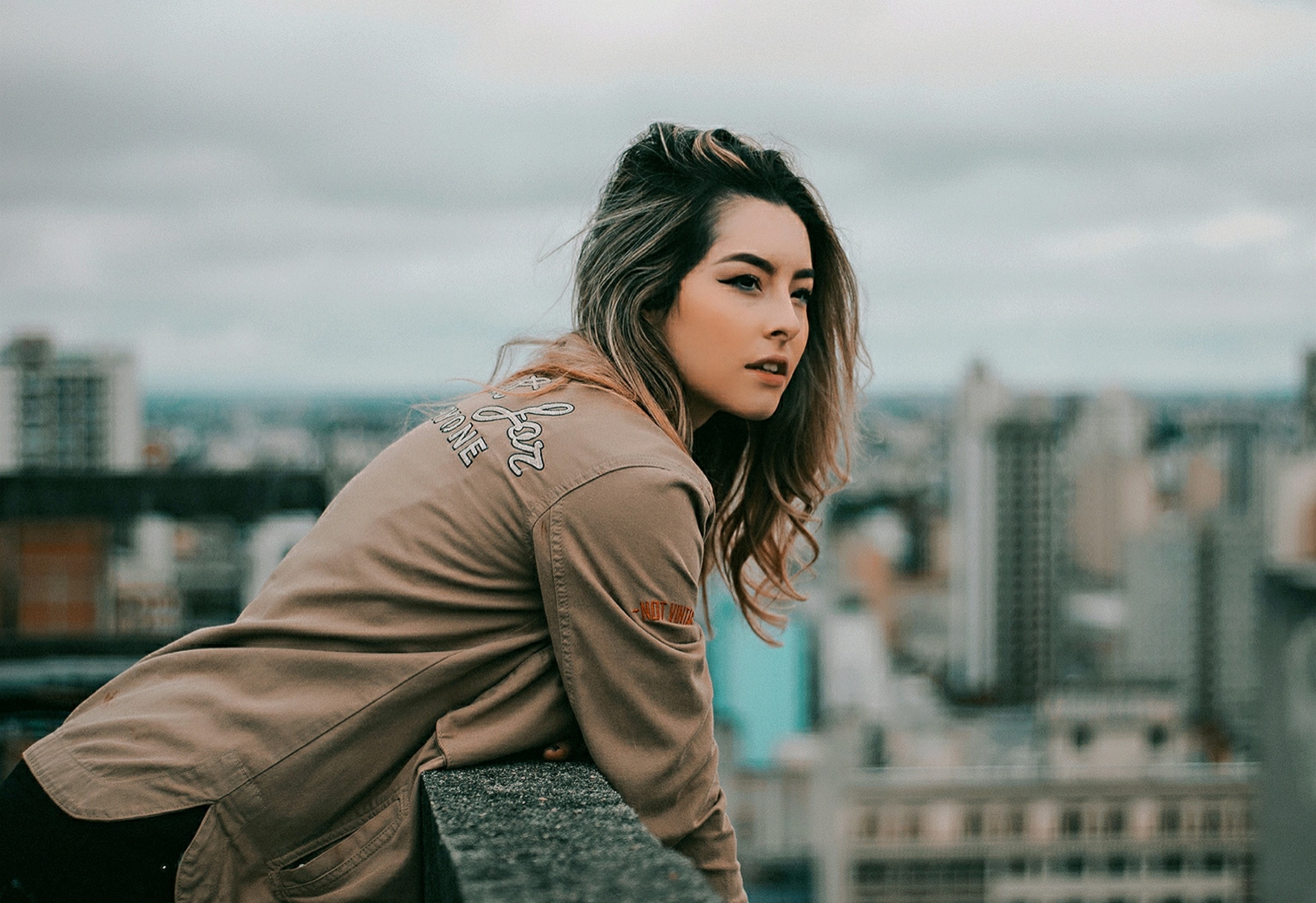 Woman leaning on a wall overlooking a city HD Wallpaper
